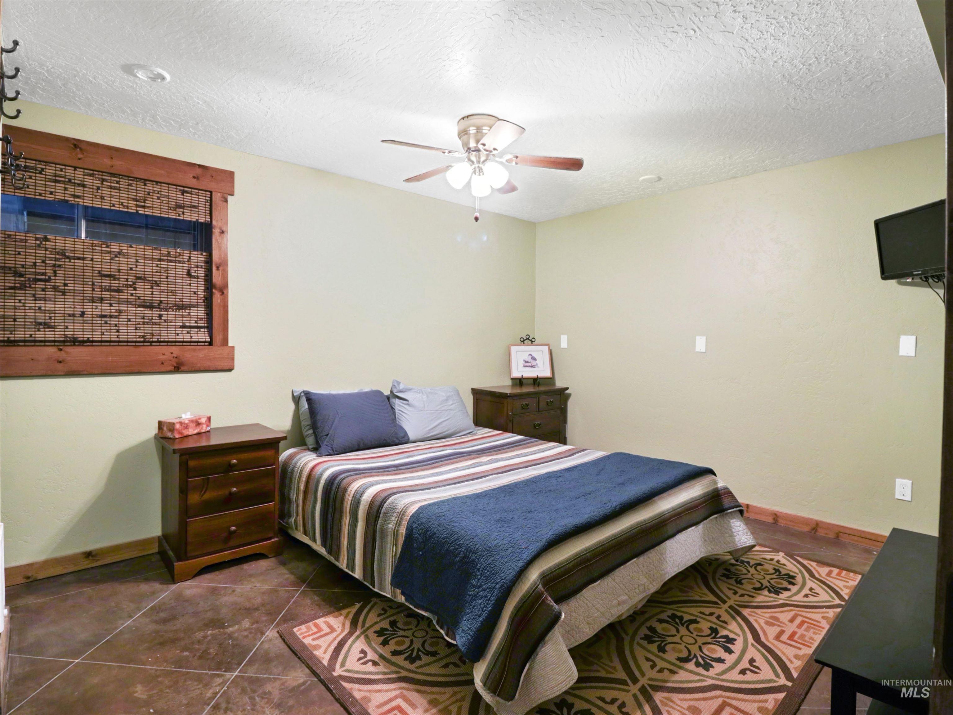 Bedroom with a textured ceiling, dark tile patterned flooring, and ceiling fan