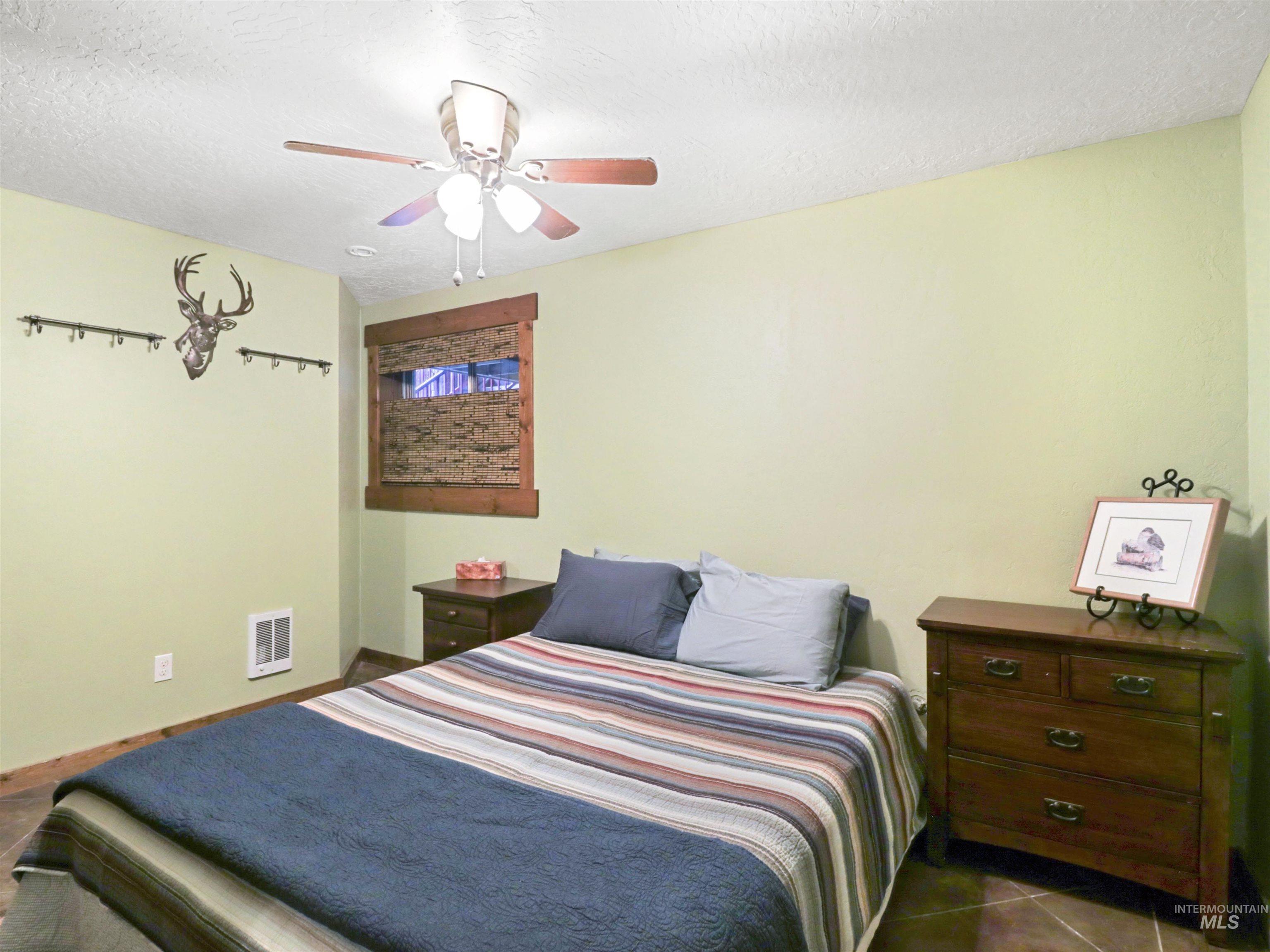 Bedroom with a textured ceiling, a ceiling fan, and dark tile patterned flooring