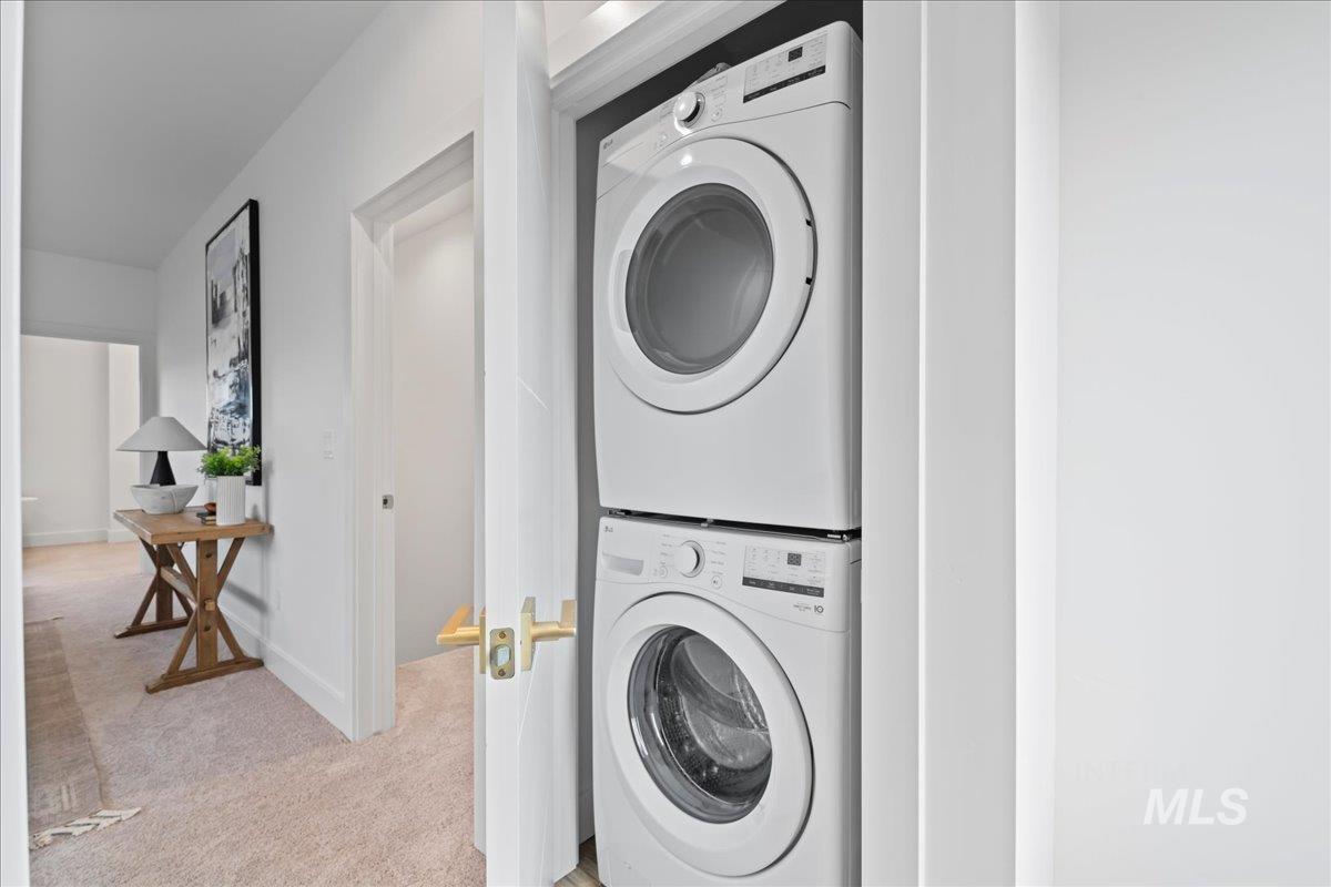 Laundry room featuring stacked washing machine and dryer and light colored carpet