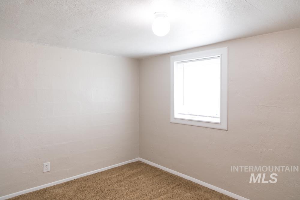 Carpeted empty room featuring a textured ceiling and baseboards