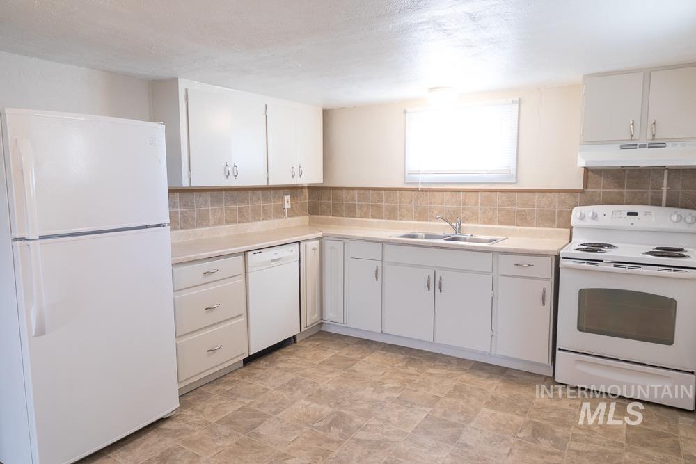 Kitchen with white appliances, light countertops, under cabinet range hood, white cabinets, and a textured ceiling