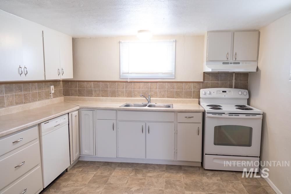 Kitchen featuring white appliances, light countertops, under cabinet range hood, tasteful backsplash, and stone finish flooring