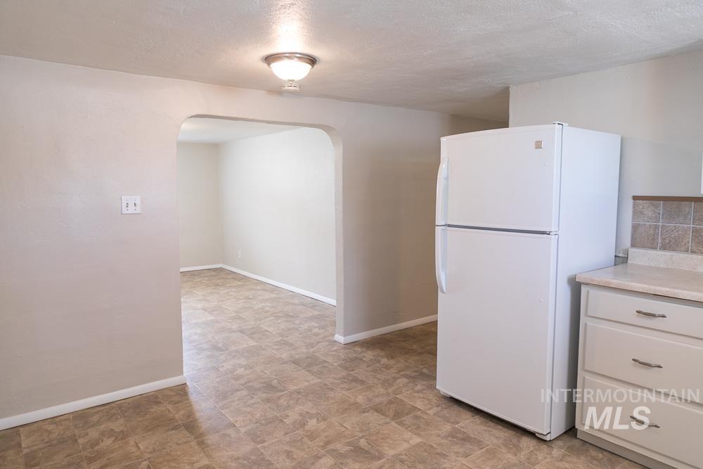 Kitchen with arched walkways, freestanding refrigerator, a textured ceiling, light countertops, and stone finish floors