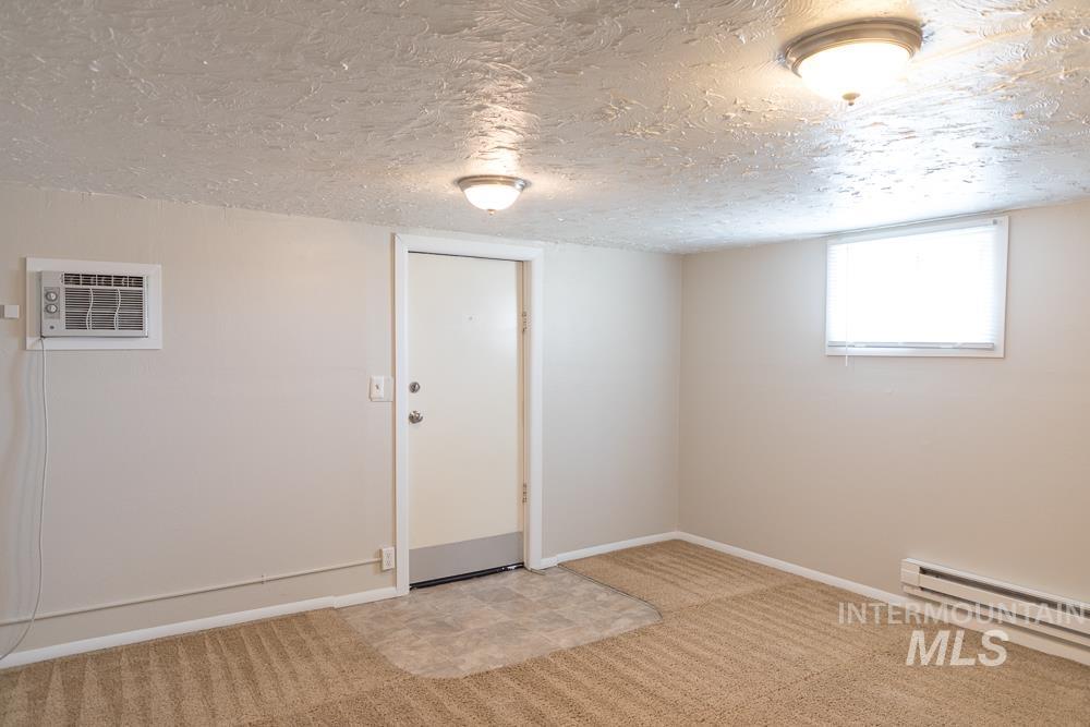 Below grade area featuring a textured ceiling, light colored carpet, and a wall unit AC