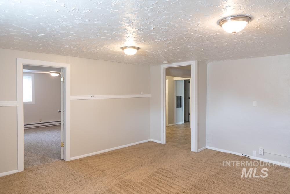 Carpeted spare room featuring a textured ceiling and a baseboard heating unit