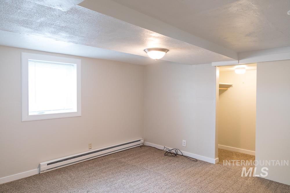 Basement with a textured ceiling, a baseboard radiator, and light carpet