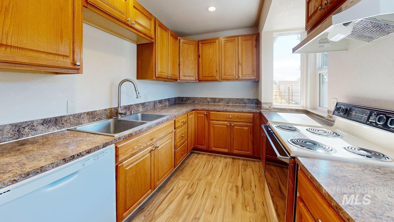 Kitchen featuring white appliances, exhaust hood, light wood-type flooring, and brown cabinets
