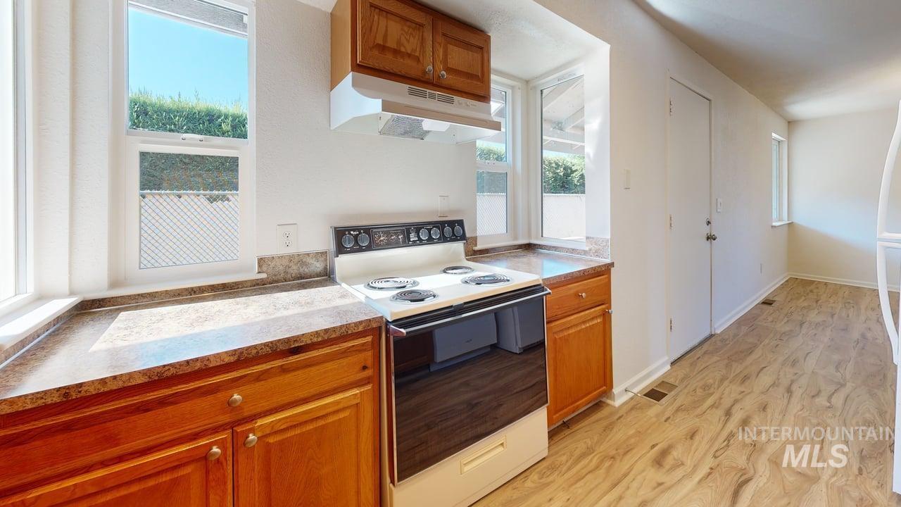 Kitchen featuring electric range, under cabinet range hood, brown cabinetry, light wood finished floors, and light countertops