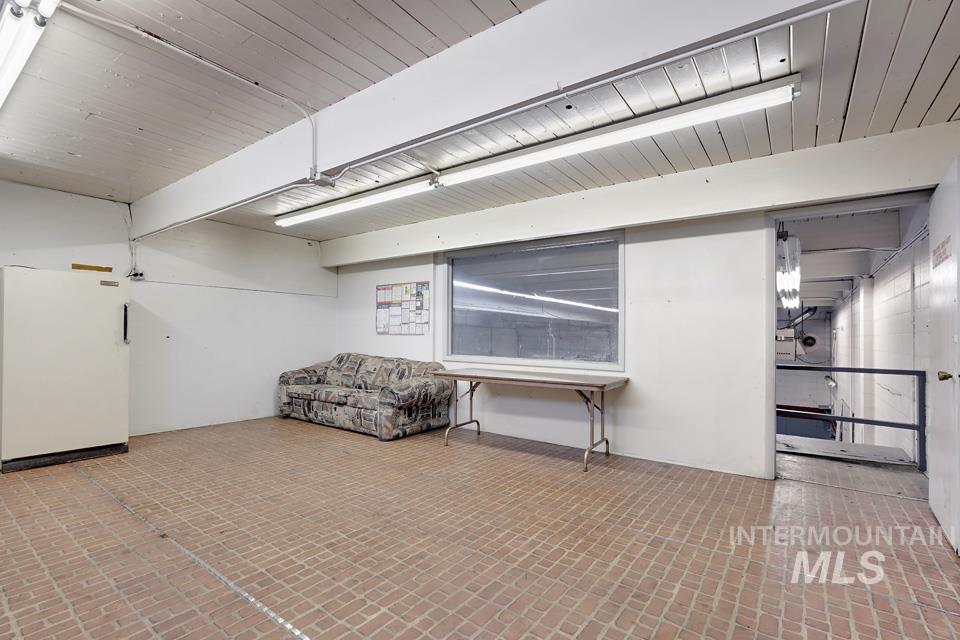 Below grade area featuring brick patterned floors, wood ceiling, and freestanding refrigerator