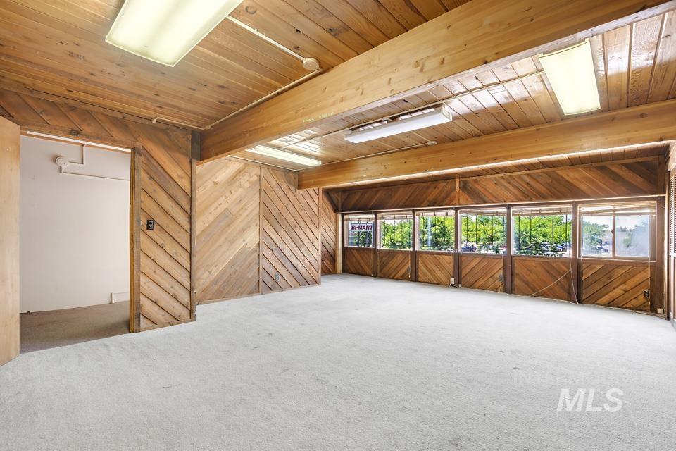 Carpeted spare room featuring a wooden ceiling with exposed beams and wooden walls