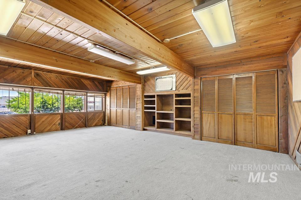 Unfurnished living room featuring a wood ceiling with exposed beams, wood walls, and carpet floors
