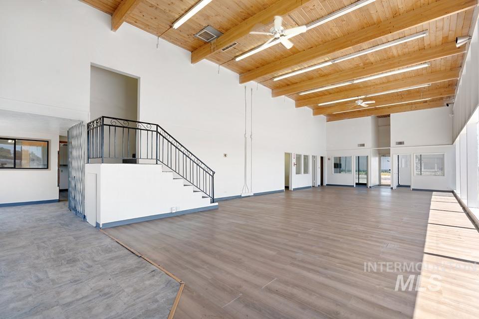 Unfurnished living room featuring a towering ceiling, a wooden ceiling with exposed beams, a ceiling fan, wood finished floors, and stairway