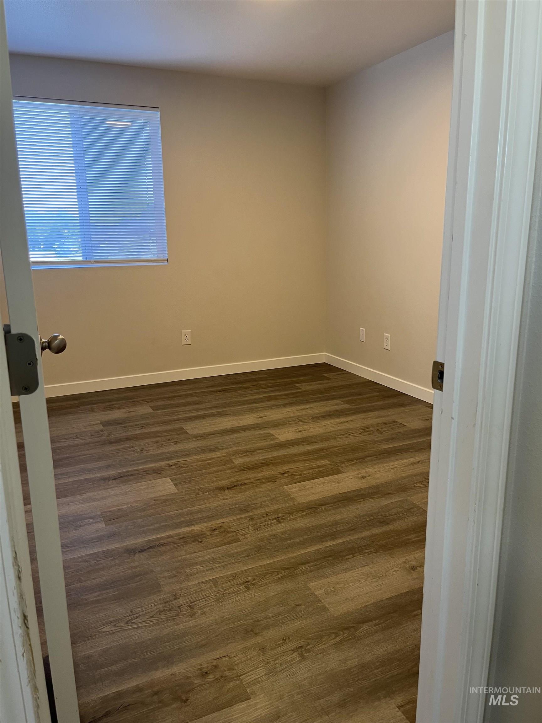 Unfurnished room featuring dark wood-style flooring and baseboards