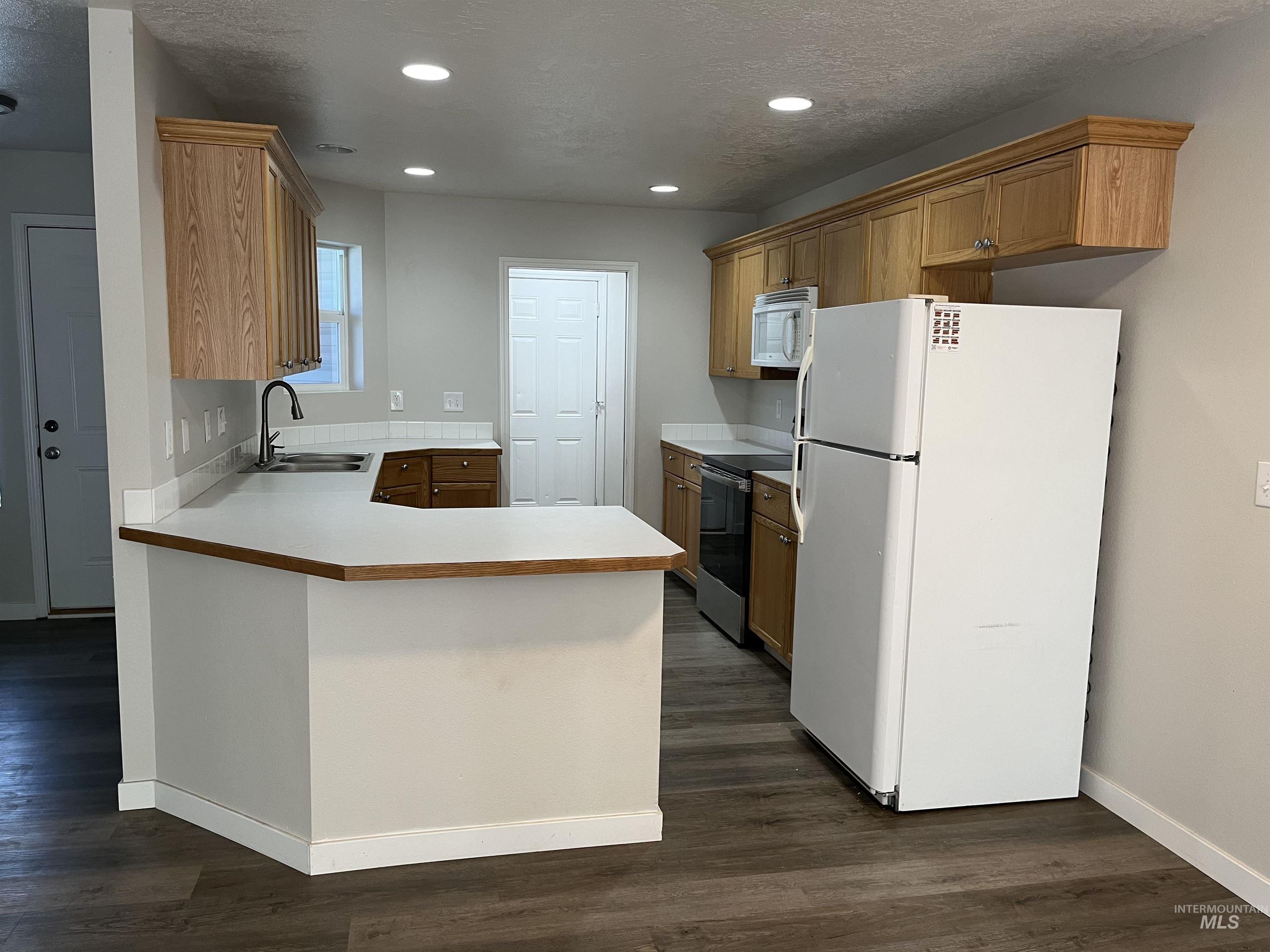 Kitchen featuring white appliances, a textured ceiling, light countertops, dark wood-type flooring, and recessed lighting