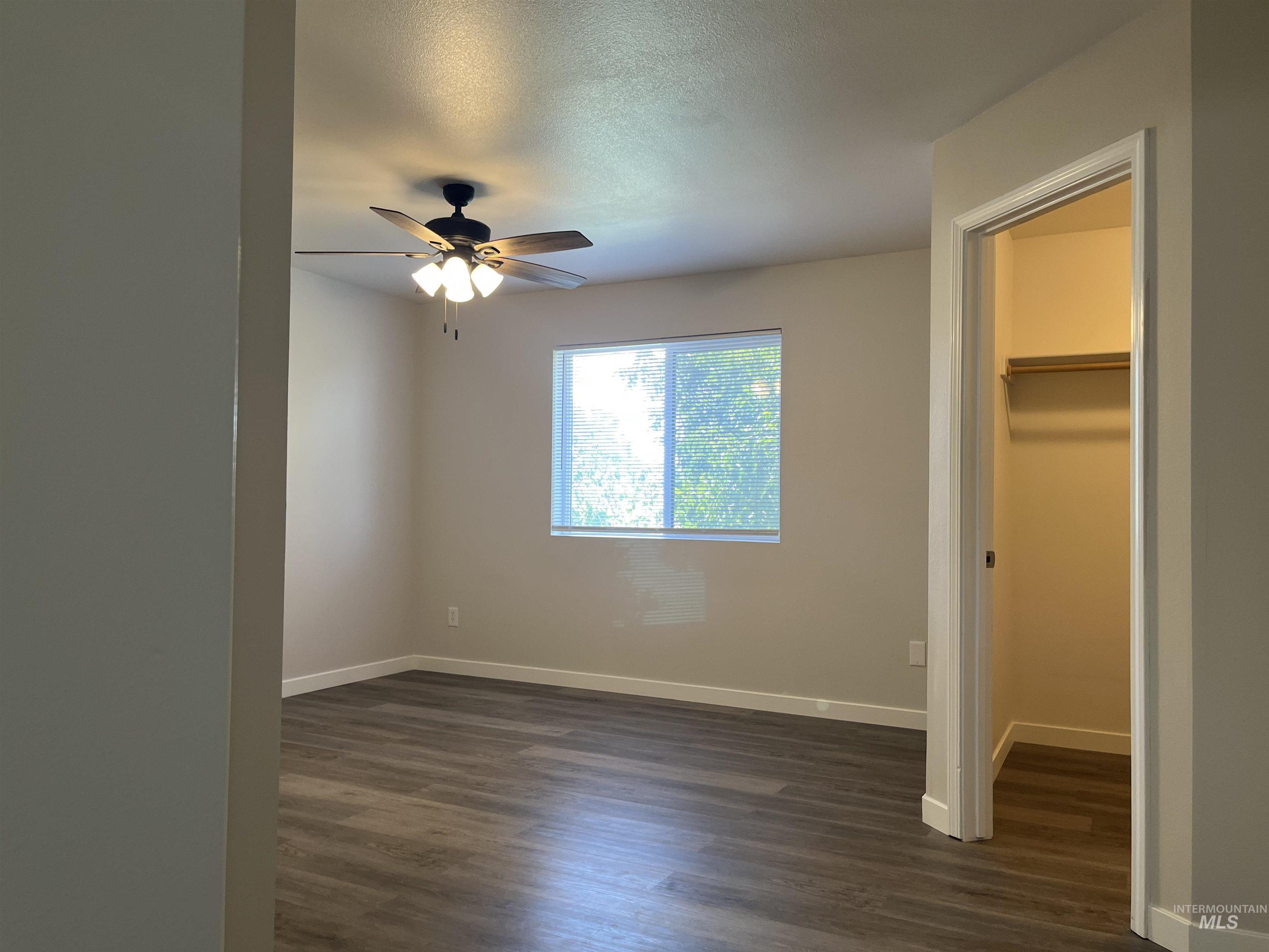 Unfurnished bedroom featuring a spacious closet, dark wood-type flooring, a textured ceiling, and ceiling fan