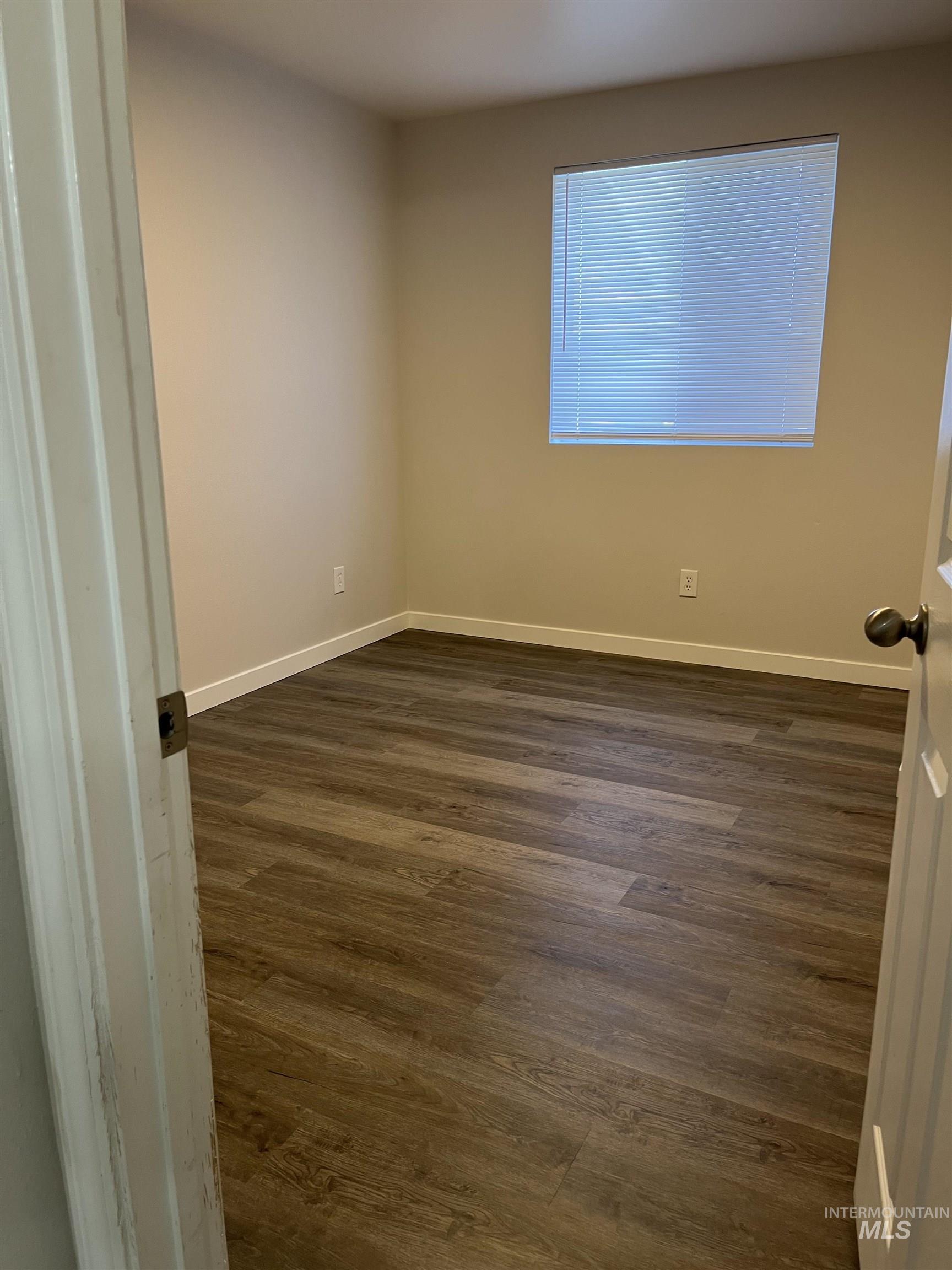 Spare room featuring dark wood-style floors and baseboards