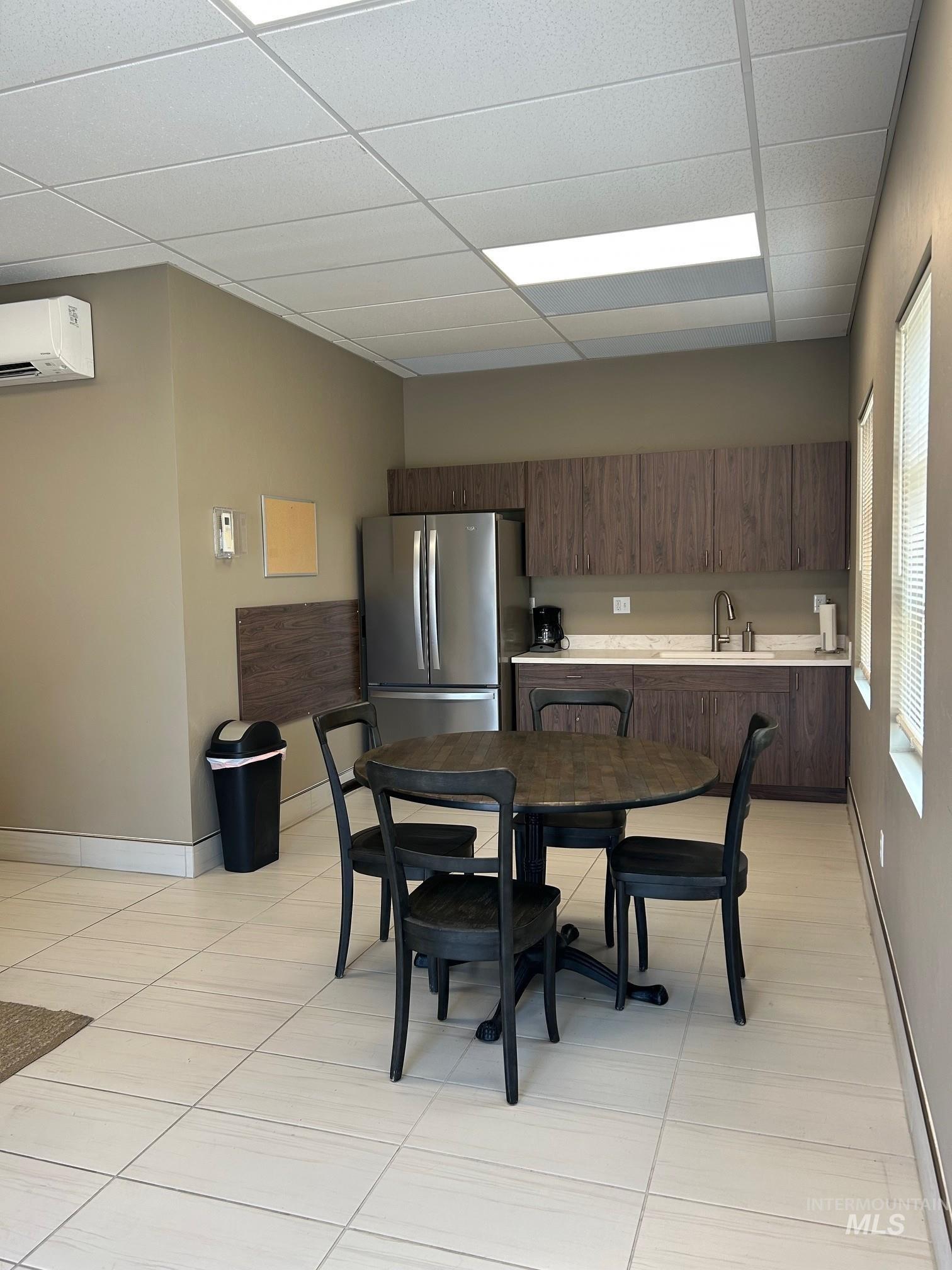 Dining area featuring a paneled ceiling, a wall mounted air conditioner, baseboard heating, and light tile patterned floors