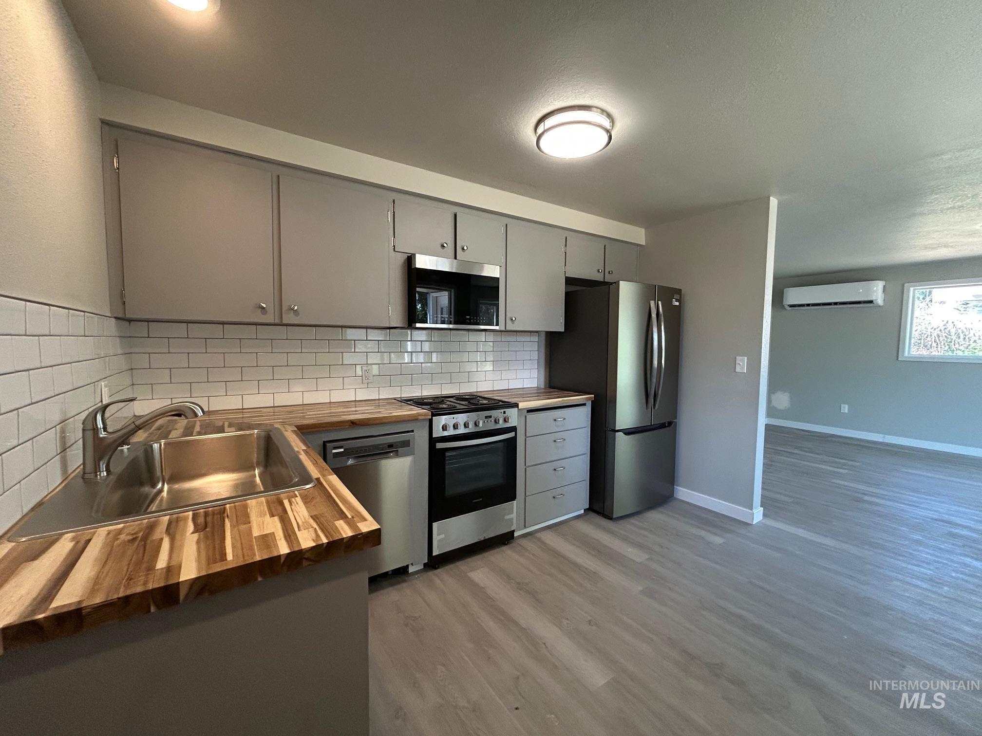 Kitchen featuring wood counters, gray cabinets, stainless steel appliances, light wood-type flooring, and decorative backsplash