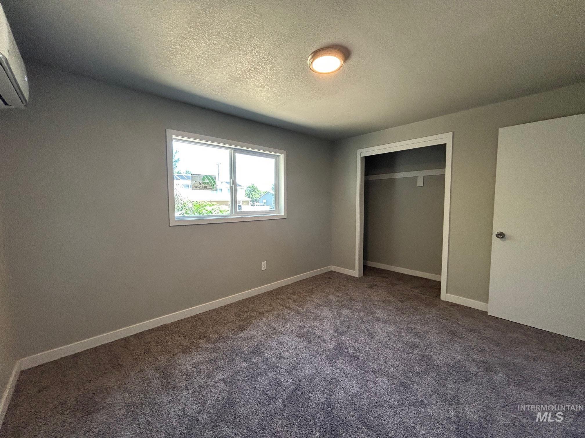 Unfurnished bedroom with carpet floors, a textured ceiling, a closet, and a wall mounted AC