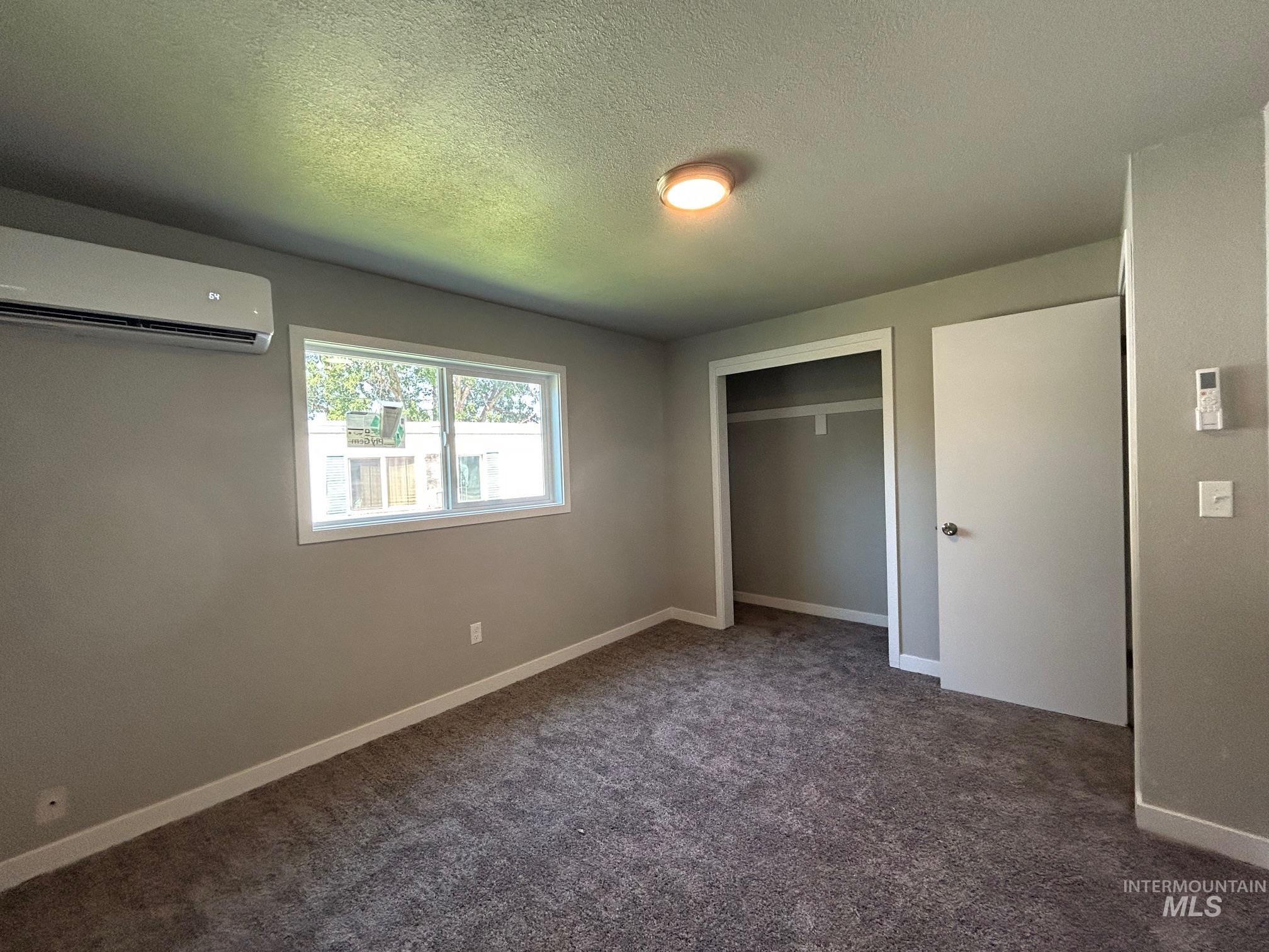 Unfurnished bedroom featuring carpet floors, a textured ceiling, a wall mounted AC, and a closet