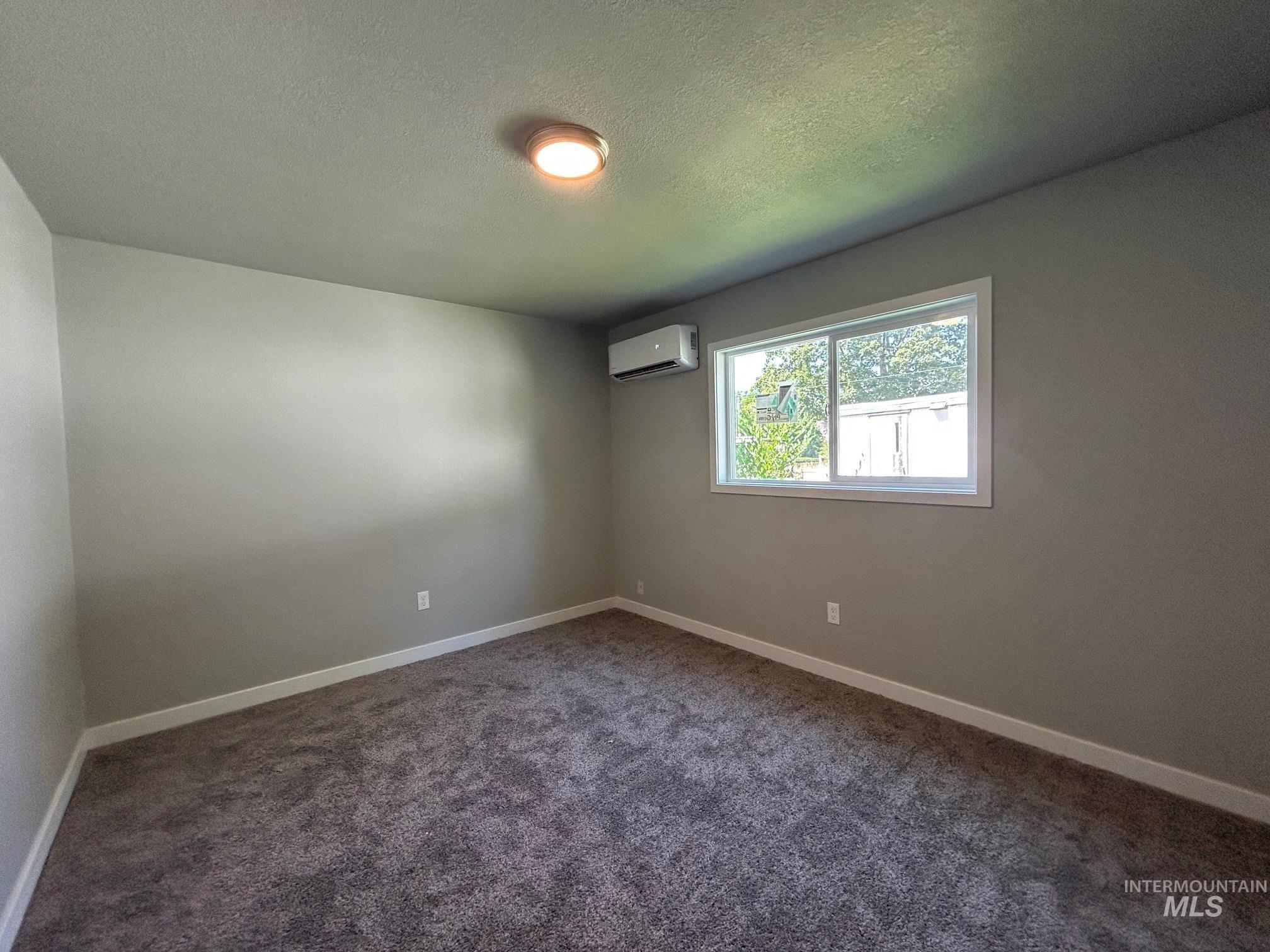 Carpeted empty room featuring a textured ceiling and a wall mounted AC