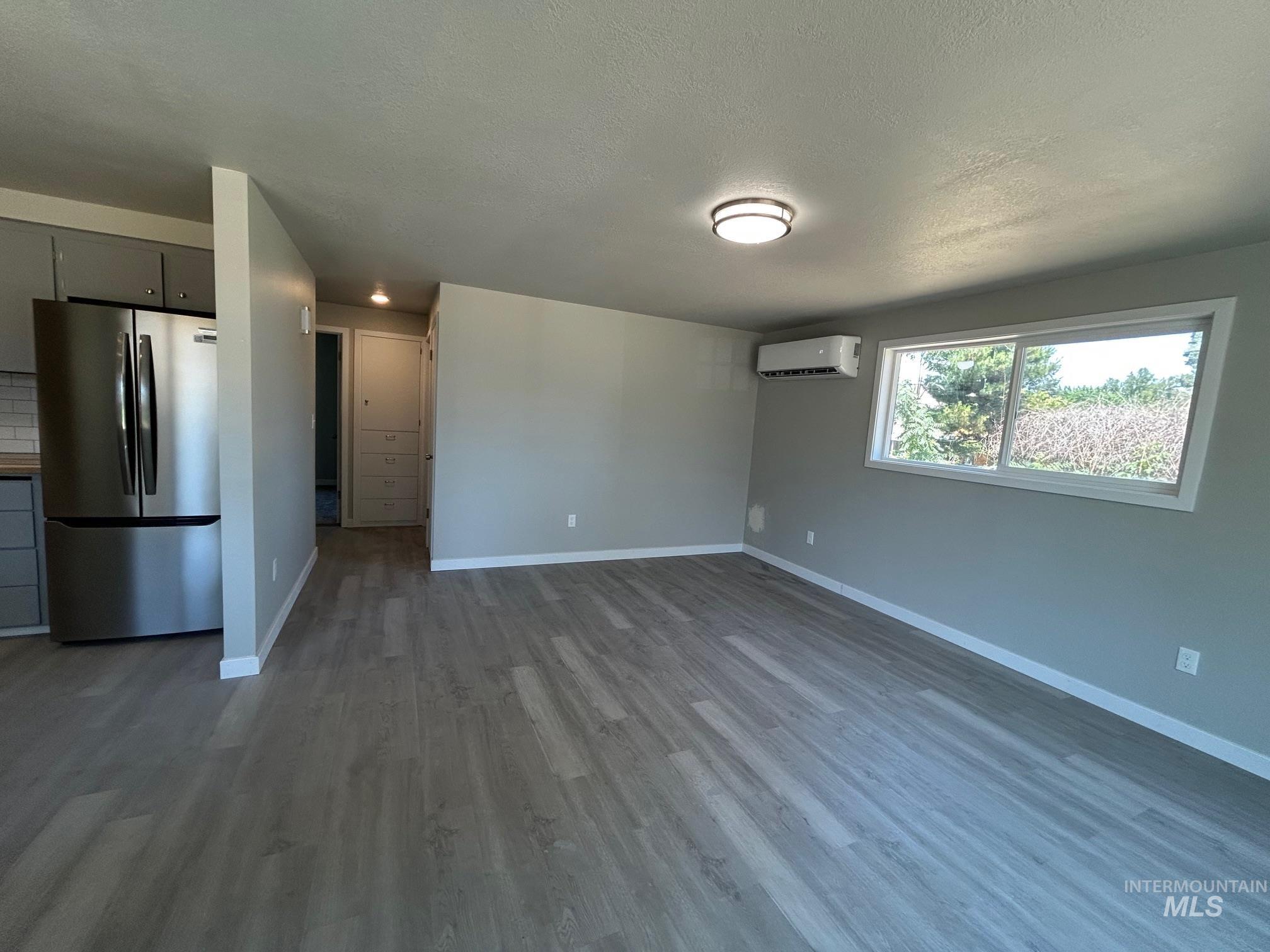 Unfurnished living room featuring wood finished floors, a textured ceiling, and a wall unit AC