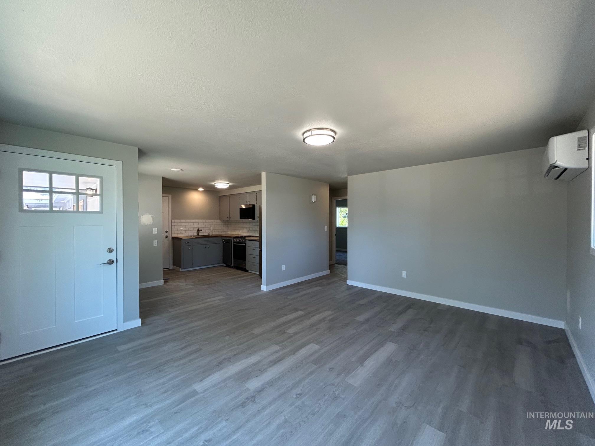 Unfurnished living room featuring wood finished floors, a wall unit AC, and a textured ceiling
