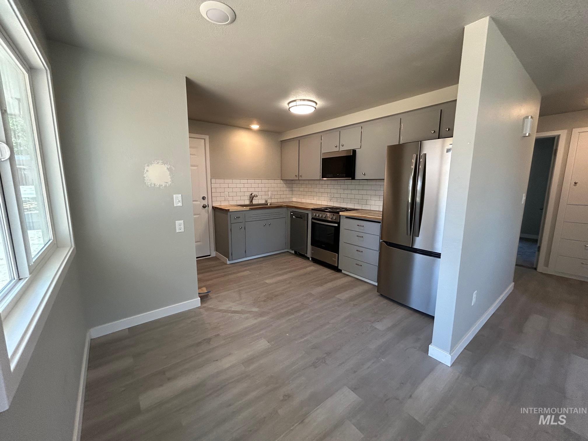 Kitchen with gray cabinets, wooden counters, stainless steel appliances, wood finished floors, and decorative backsplash