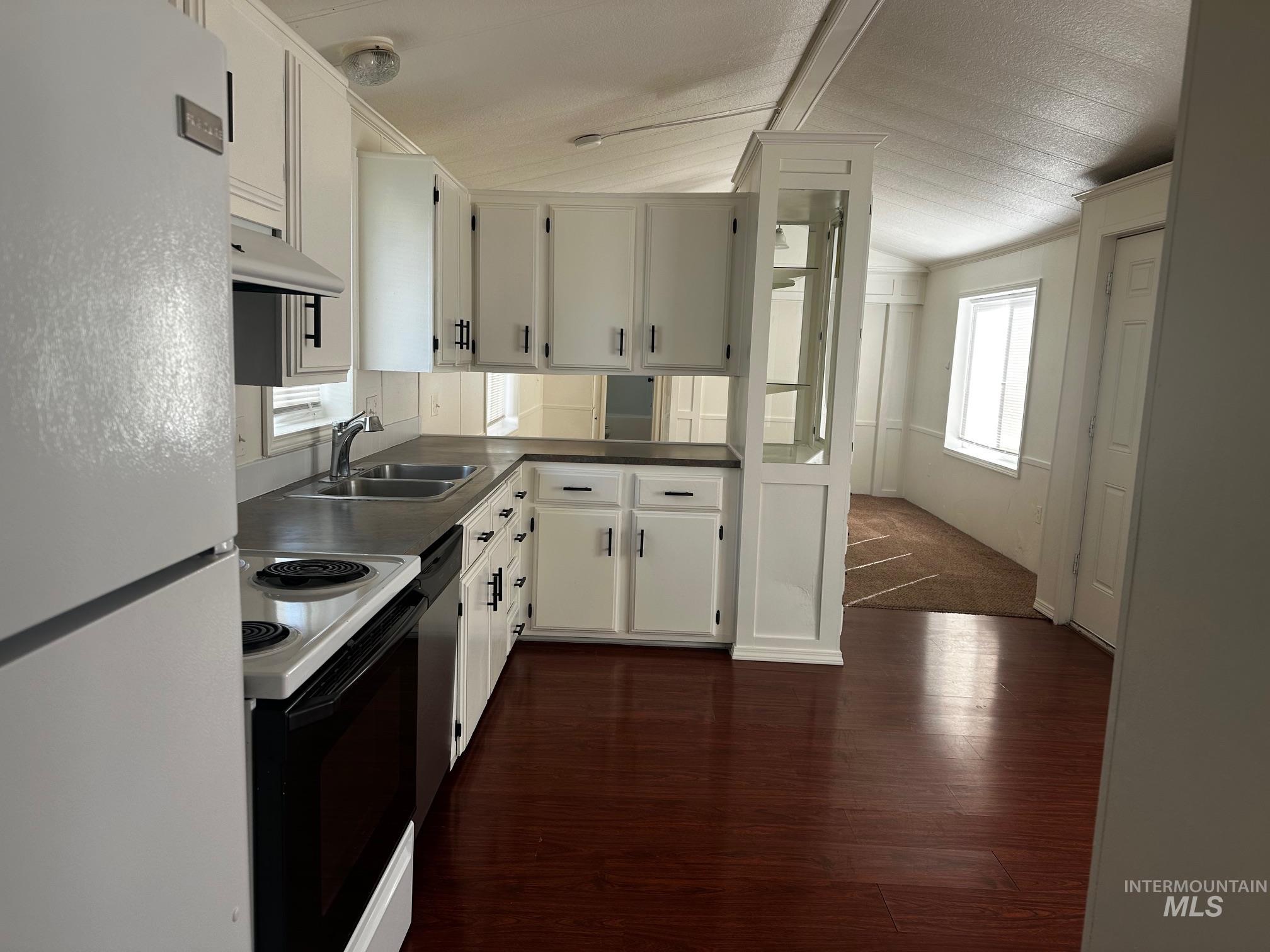 Kitchen featuring white appliances, white cabinets, vaulted ceiling, dark wood-type flooring, and under cabinet range hood