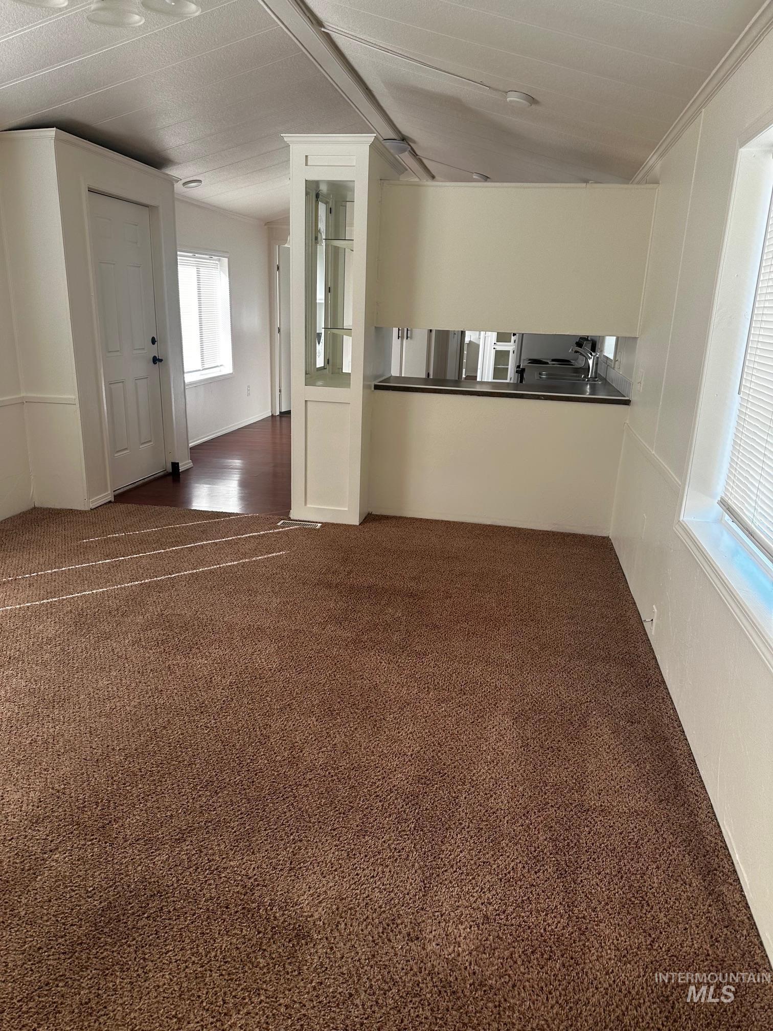 Unfurnished living room featuring dark colored carpet and crown molding