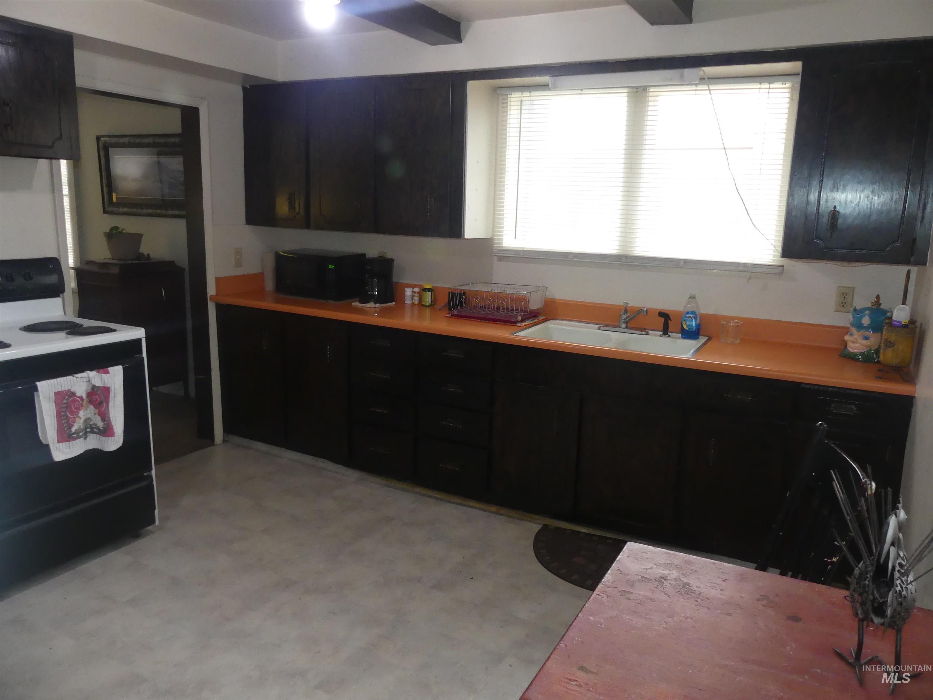 Kitchen featuring electric range, light flooring, dark cabinets, light countertops, and black microwave