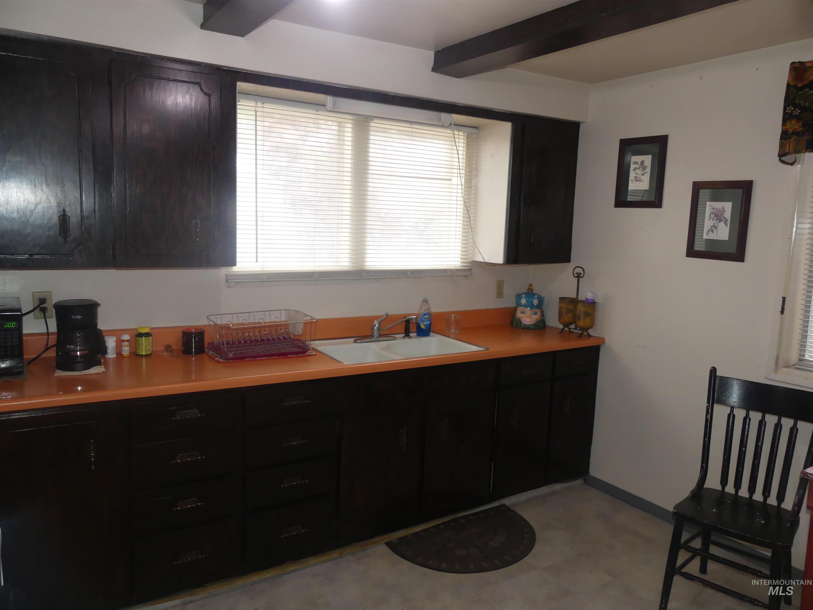 Kitchen with light countertops, beamed ceiling, and dark cabinets
