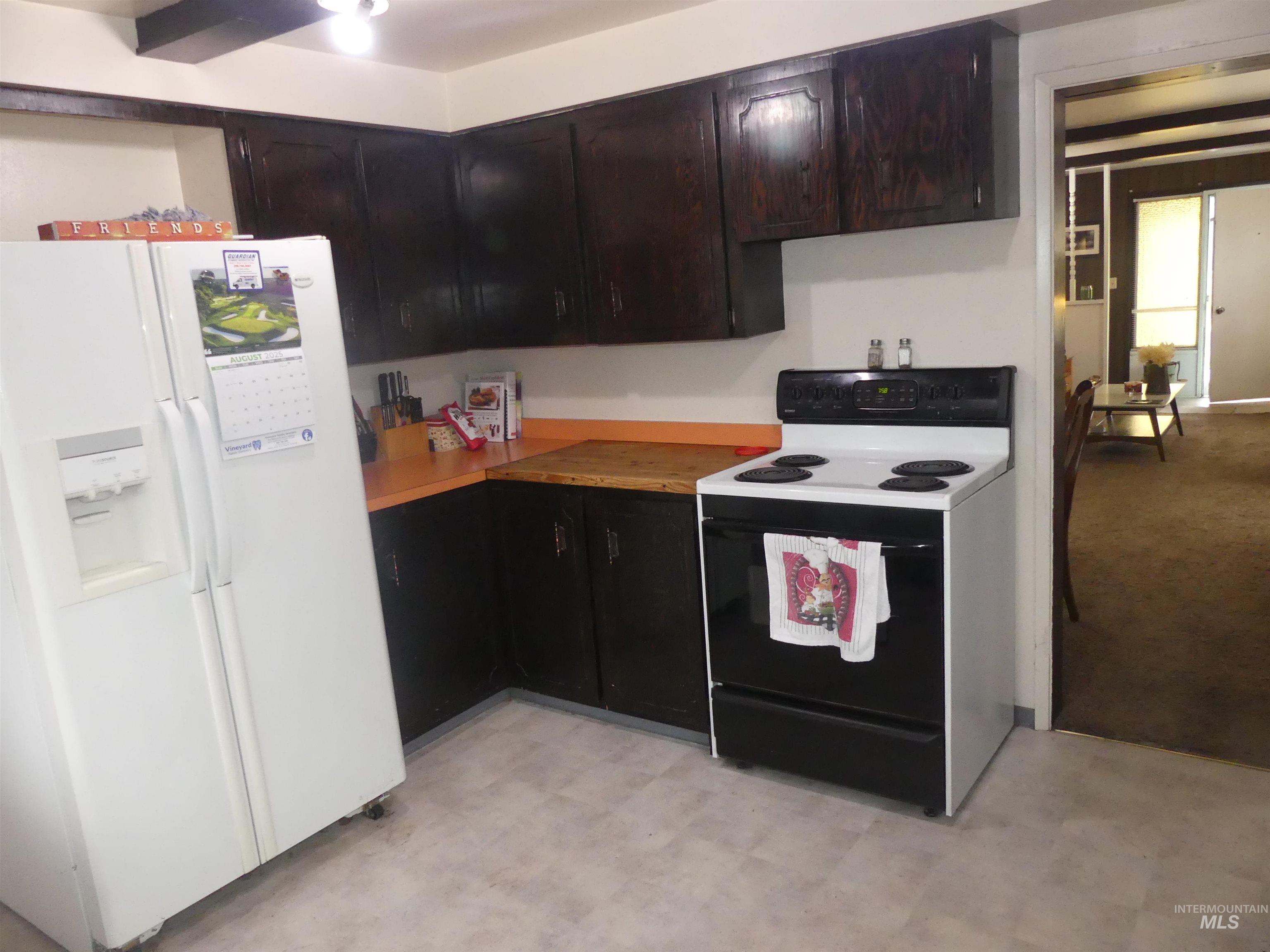 Kitchen featuring white fridge with ice dispenser, range with electric stovetop, light floors, light countertops, and dark brown cabinetry