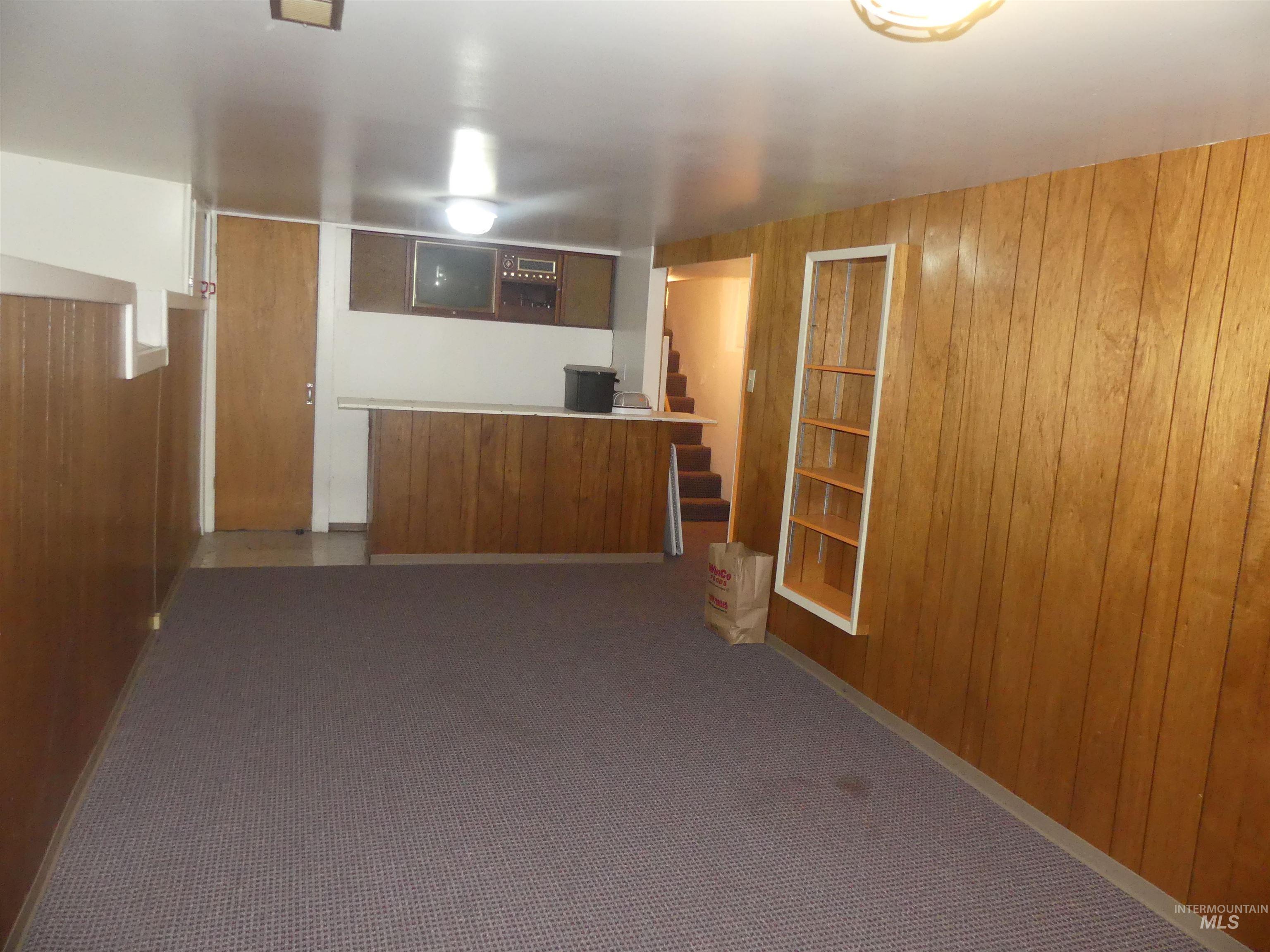 Unfurnished living room with wood walls, carpet floors, and stairway