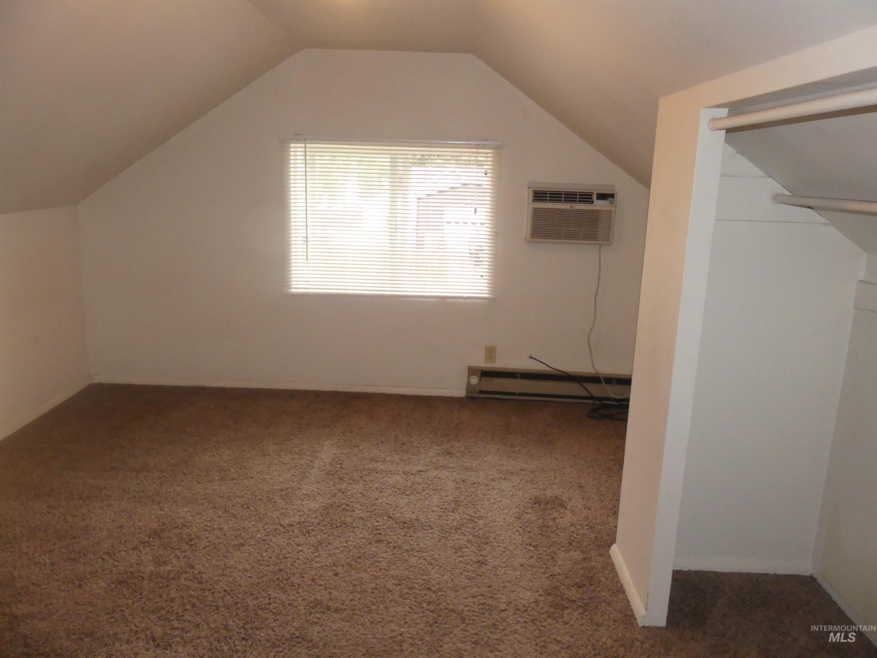 Additional living space featuring carpet flooring, lofted ceiling, an AC wall unit, and a baseboard heating unit