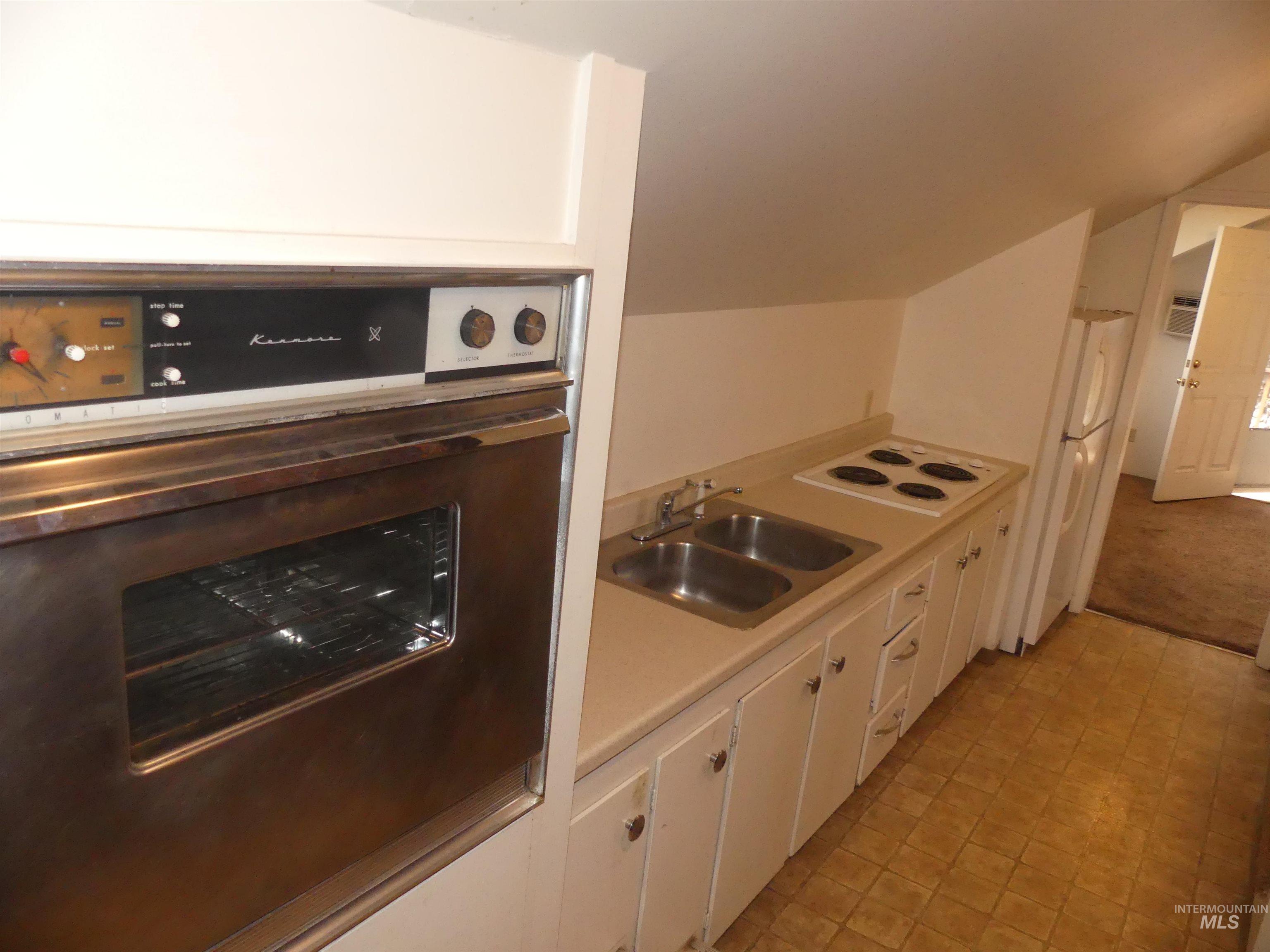 Kitchen featuring white cabinetry, white appliances, light countertops, and vaulted ceiling