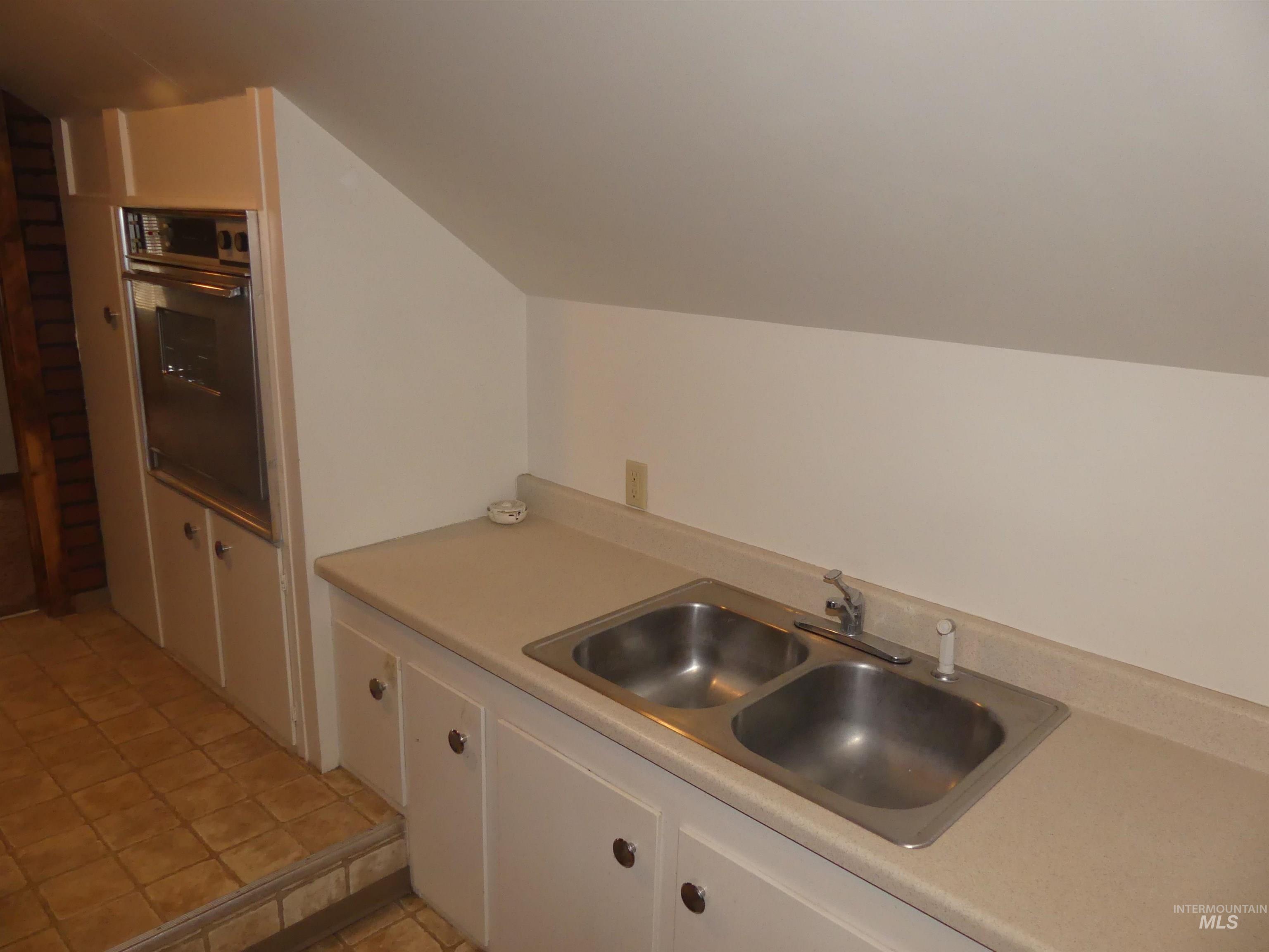 Kitchen with oven, white cabinets, light countertops, and lofted ceiling