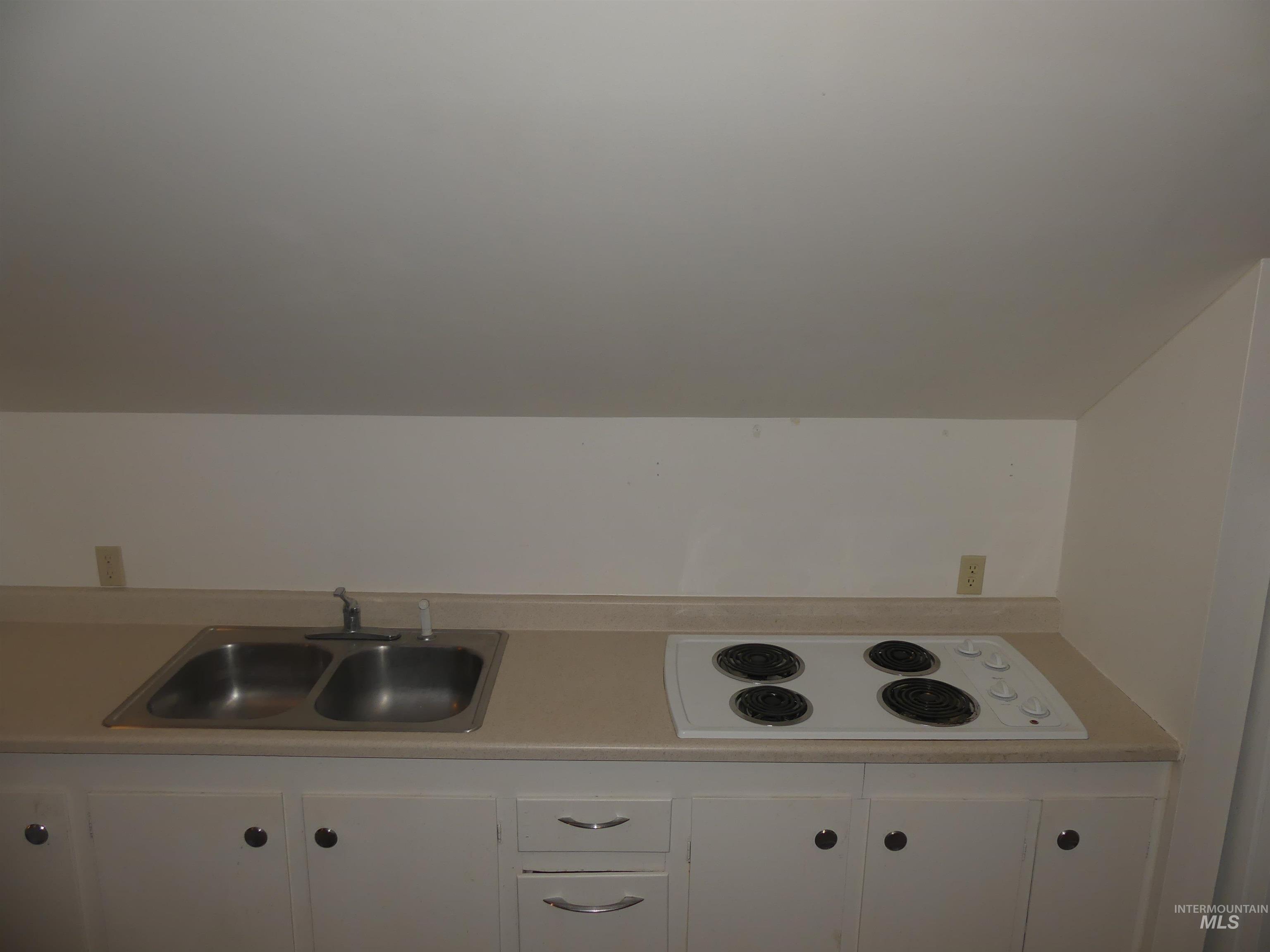 Kitchen featuring white electric cooktop, white cabinetry, light countertops, and lofted ceiling