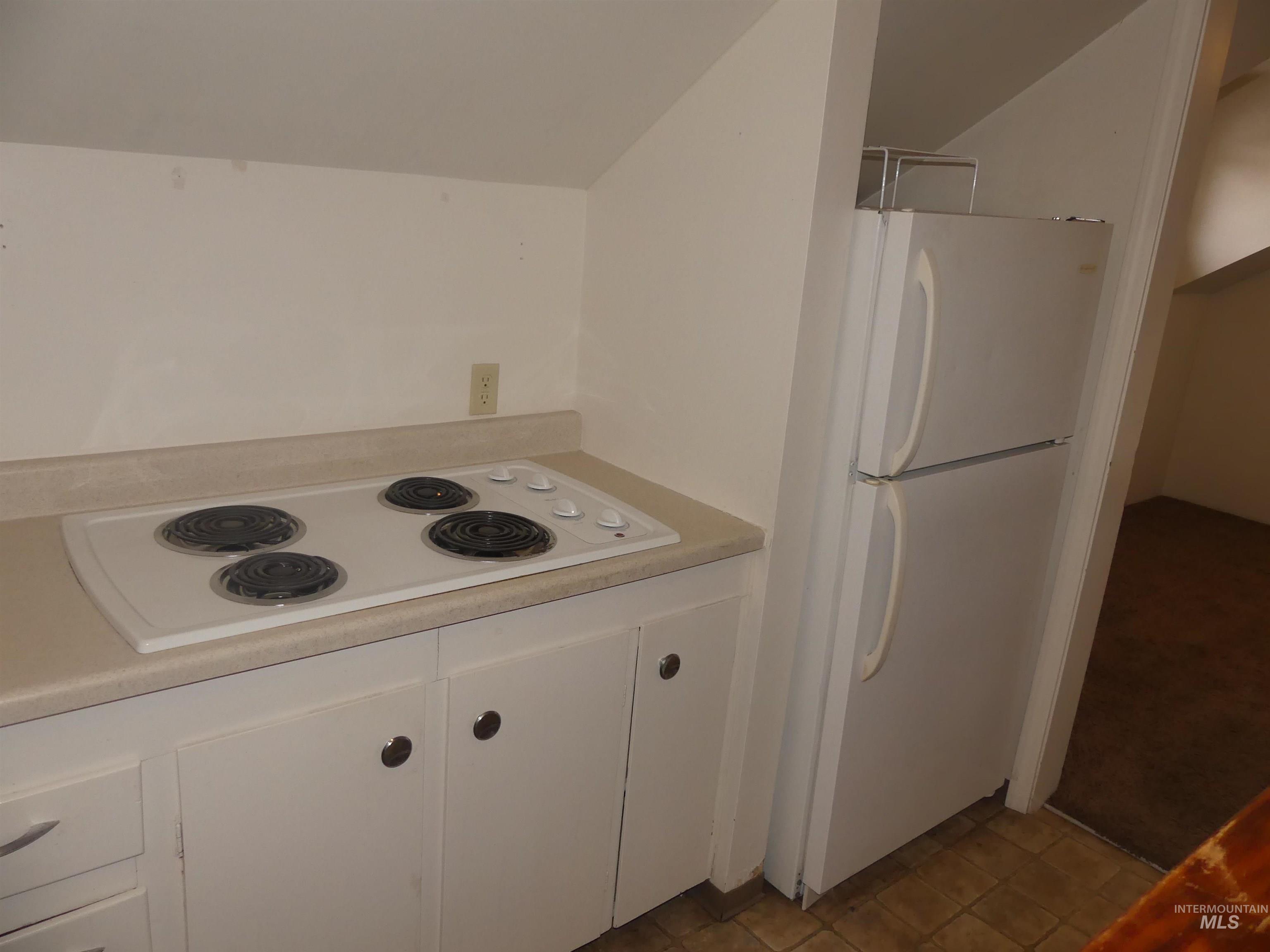 Kitchen featuring white appliances, white cabinets, light countertops, lofted ceiling, and tile patterned floors