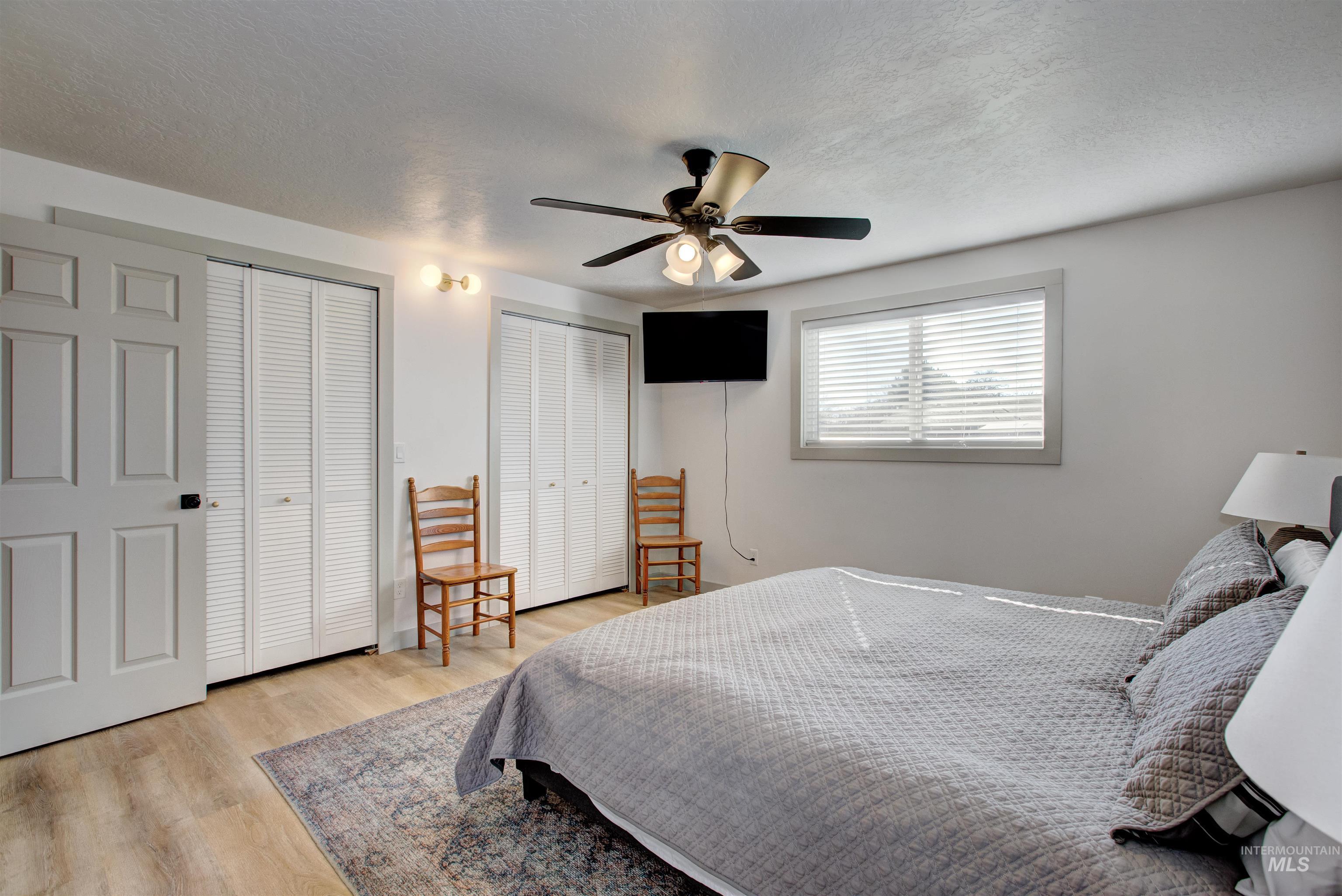 Bedroom with a textured ceiling, multiple closets, light wood-style floors, and ceiling fan