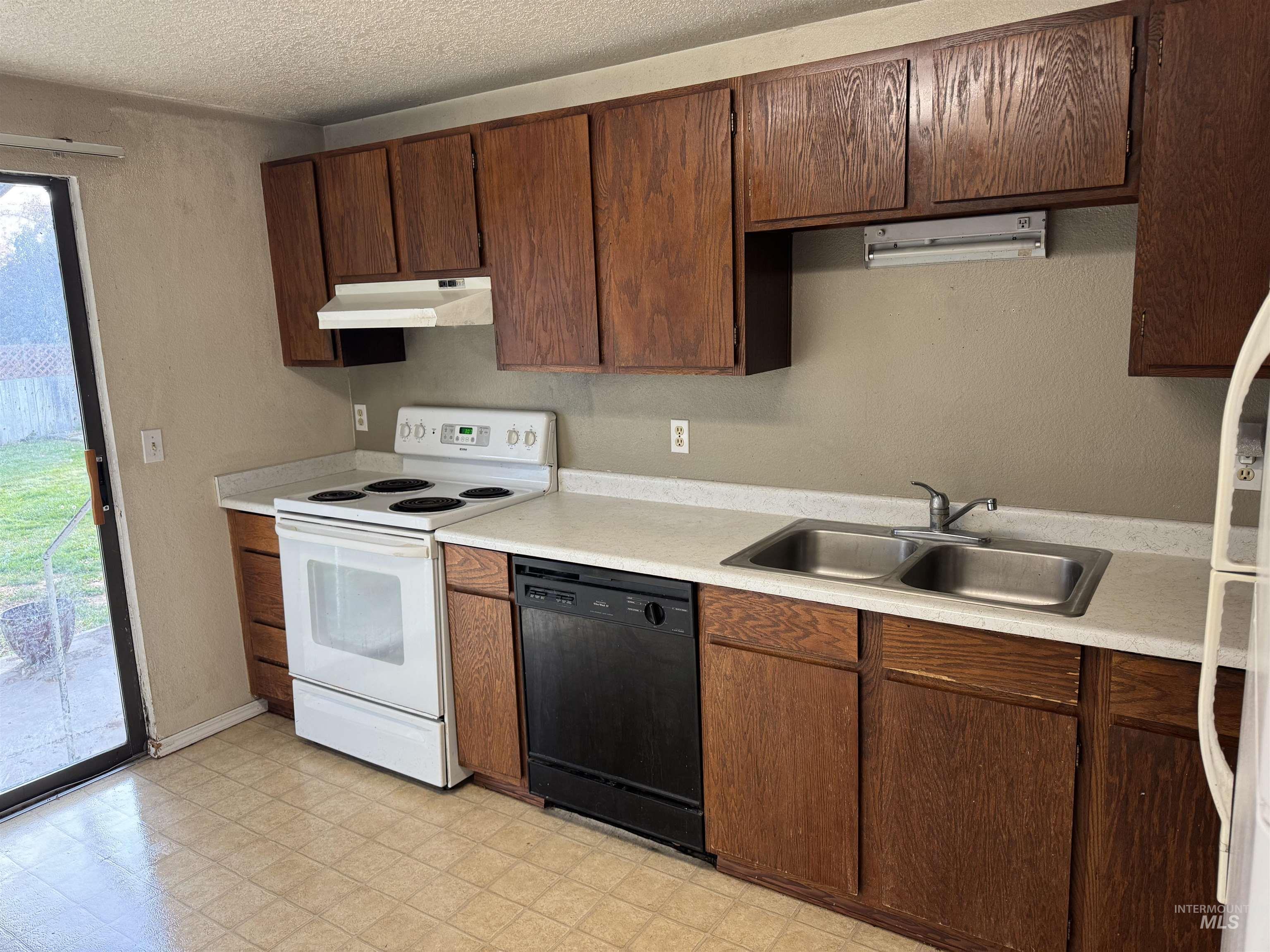 Kitchen featuring white appliances, light countertops, light flooring, under cabinet range hood, and a textured ceiling