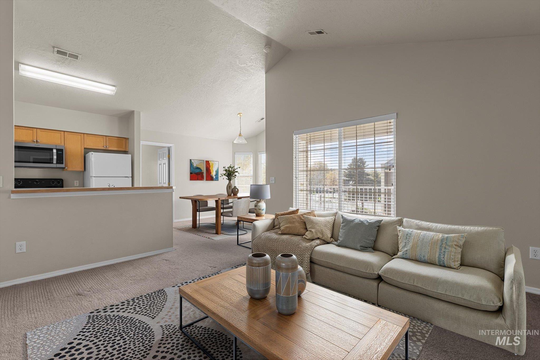 Living area featuring carpet flooring, a textured ceiling, and high vaulted ceiling