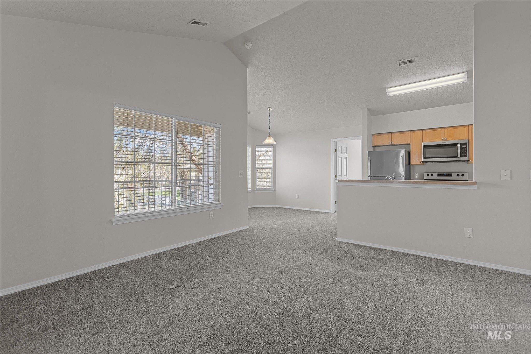 Unfurnished living room featuring carpet flooring, a textured ceiling, and high vaulted ceiling