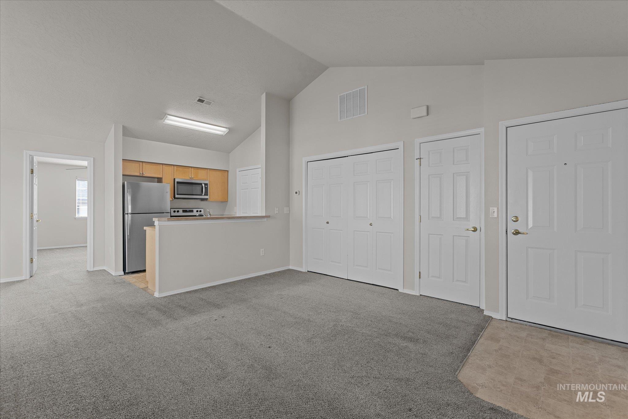 Kitchen featuring light carpet, appliances with stainless steel finishes, light brown cabinets, light countertops, and a peninsula