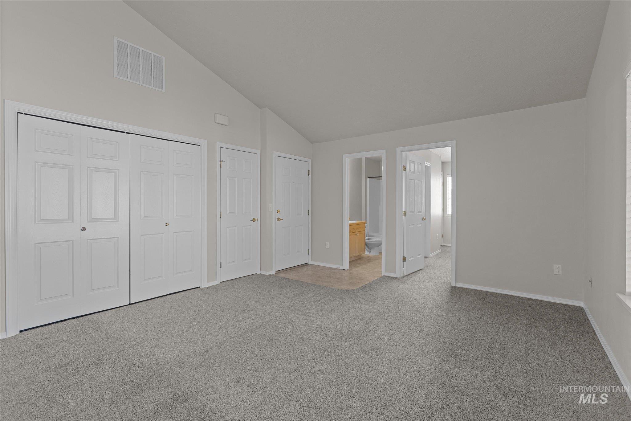 Unfurnished bedroom featuring carpet flooring, high vaulted ceiling, multiple closets, and ensuite bath