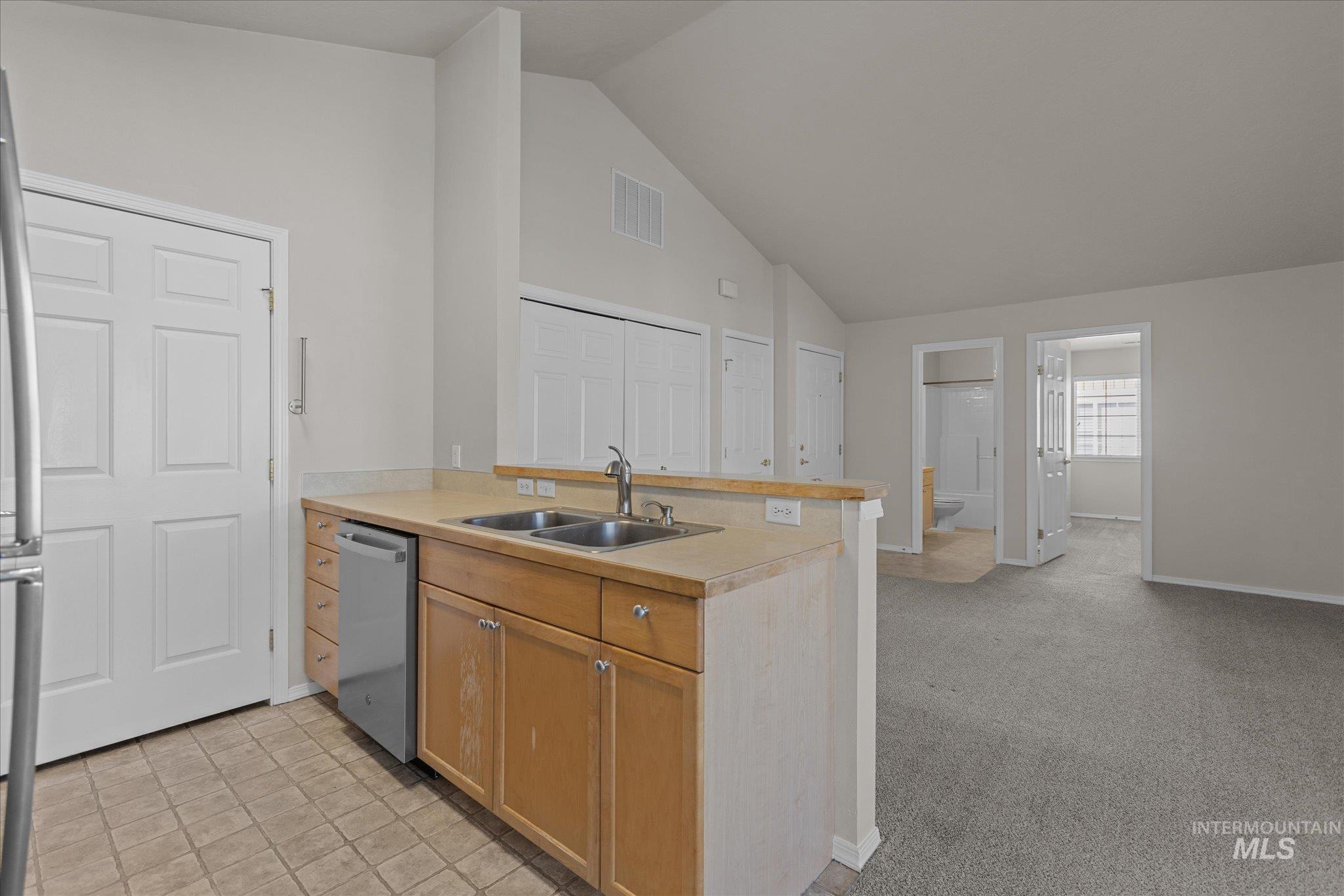 Kitchen featuring high vaulted ceiling, a peninsula, stainless steel appliances, light countertops, and light colored carpet