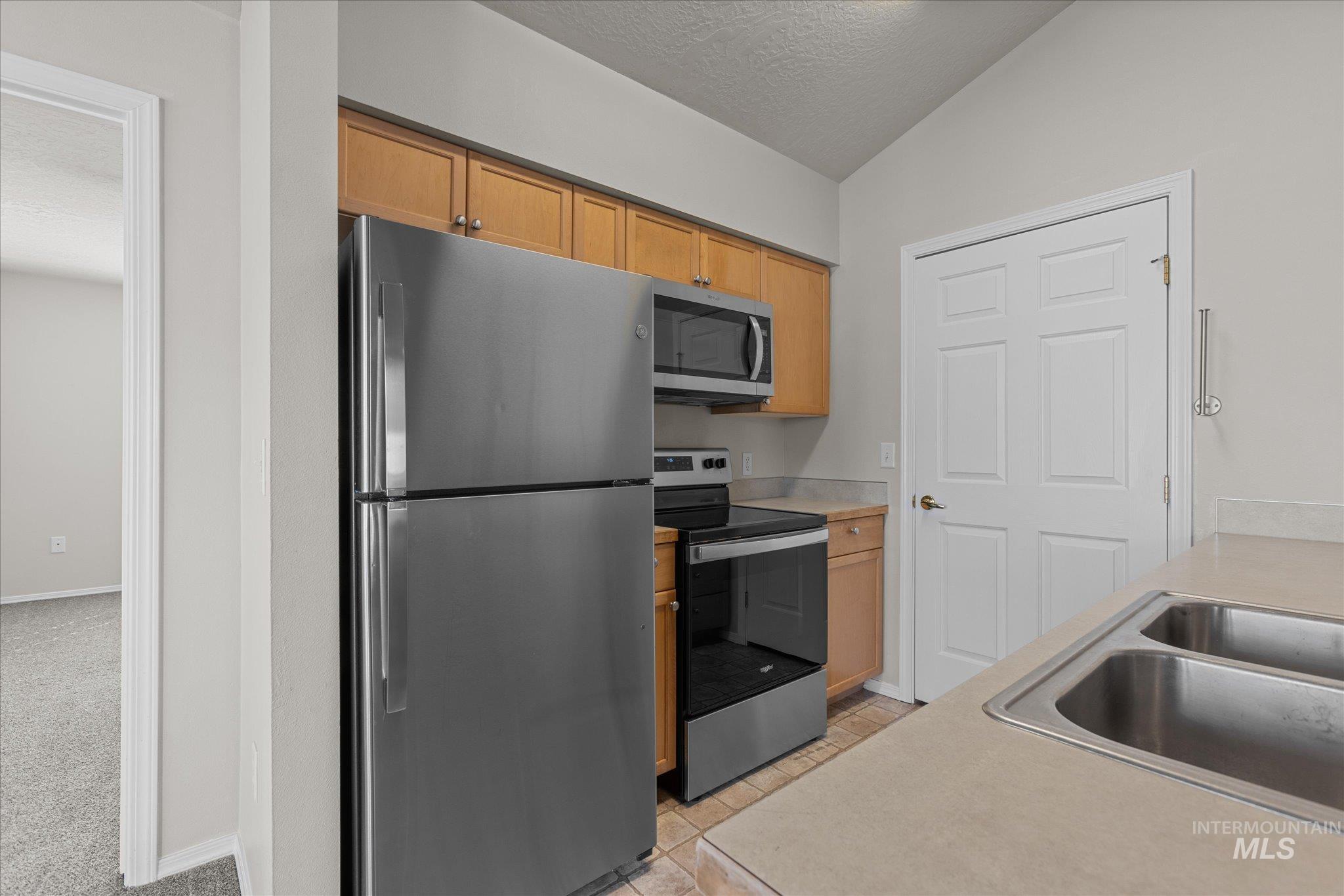 Kitchen with appliances with stainless steel finishes, a textured ceiling, vaulted ceiling, light countertops, and light tile patterned floors