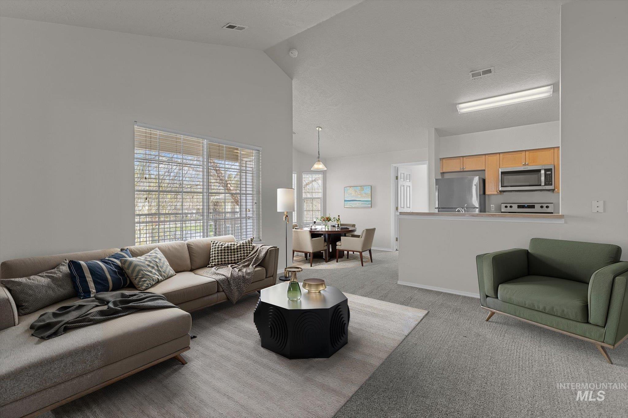 Living room with light colored carpet, a textured ceiling, and high vaulted ceiling