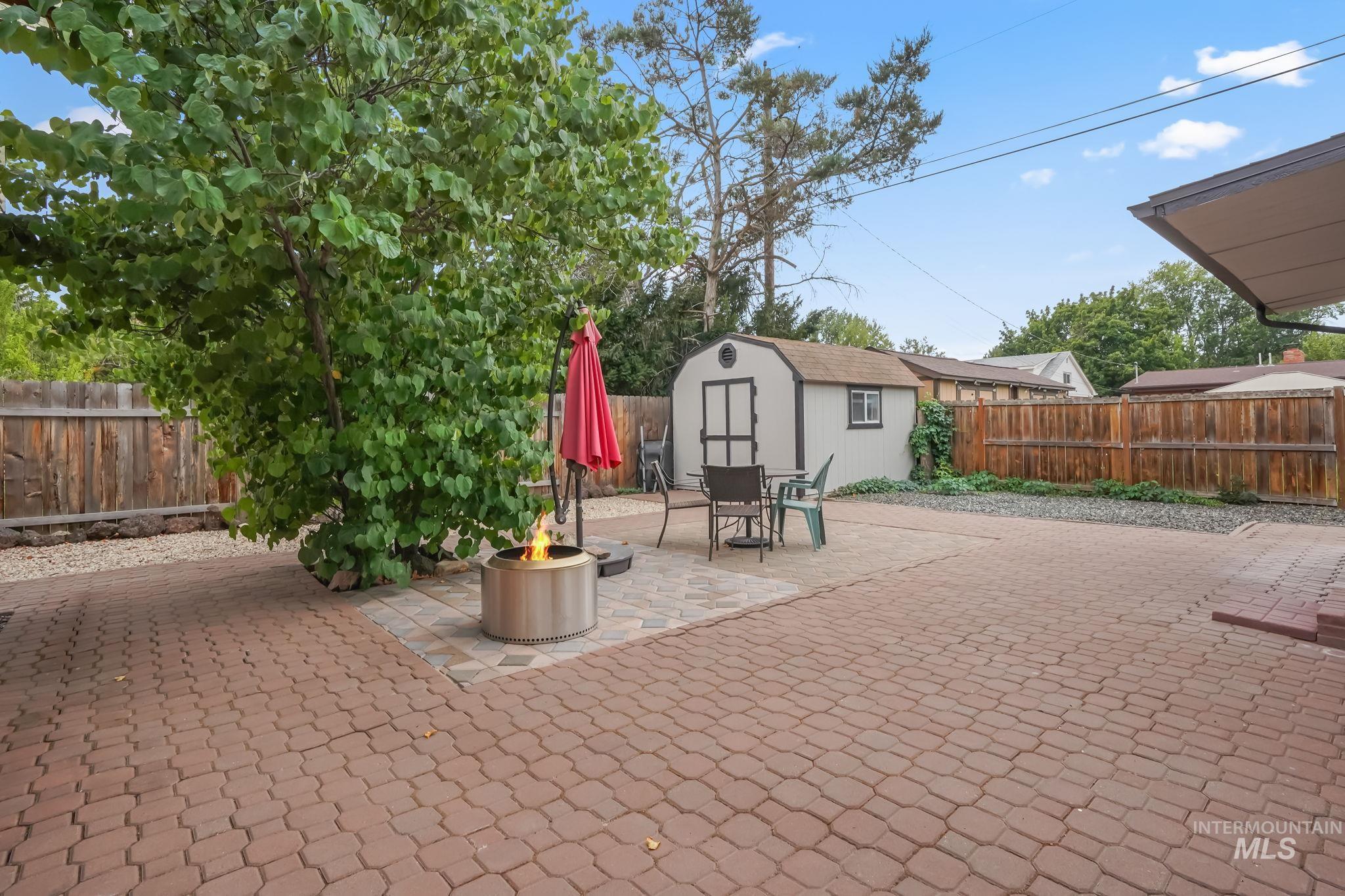 Fenced backyard with a storage unit, a patio area, an outdoor fire pit, and outdoor dining space