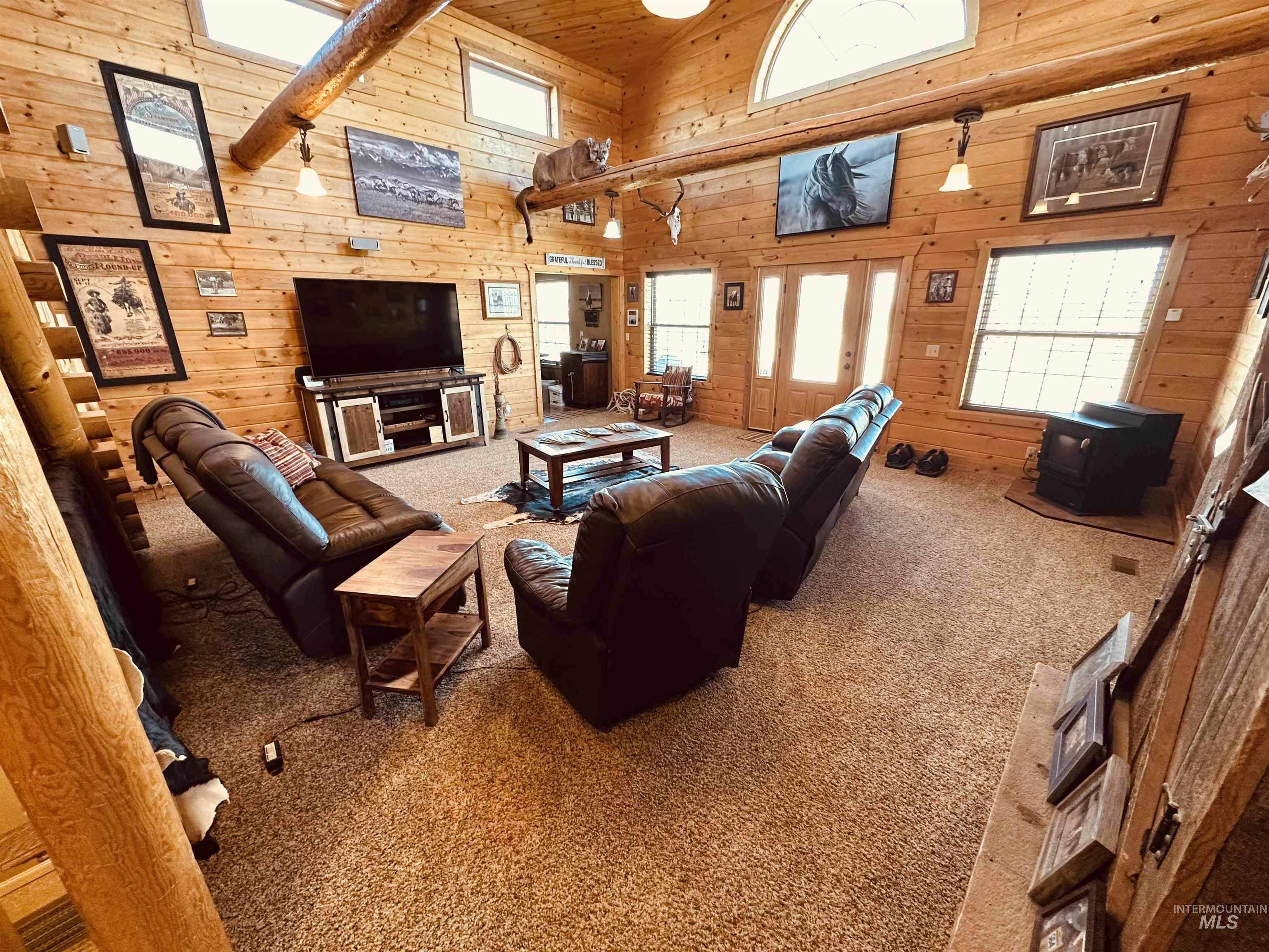 Living area with high vaulted ceiling, a wood stove, wooden walls, carpet flooring, and french doors